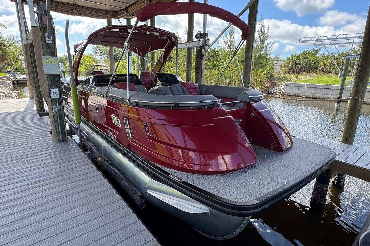 2024 Bennington QX27 pontoon boat docked, featuring sleek red design and spacious seating.