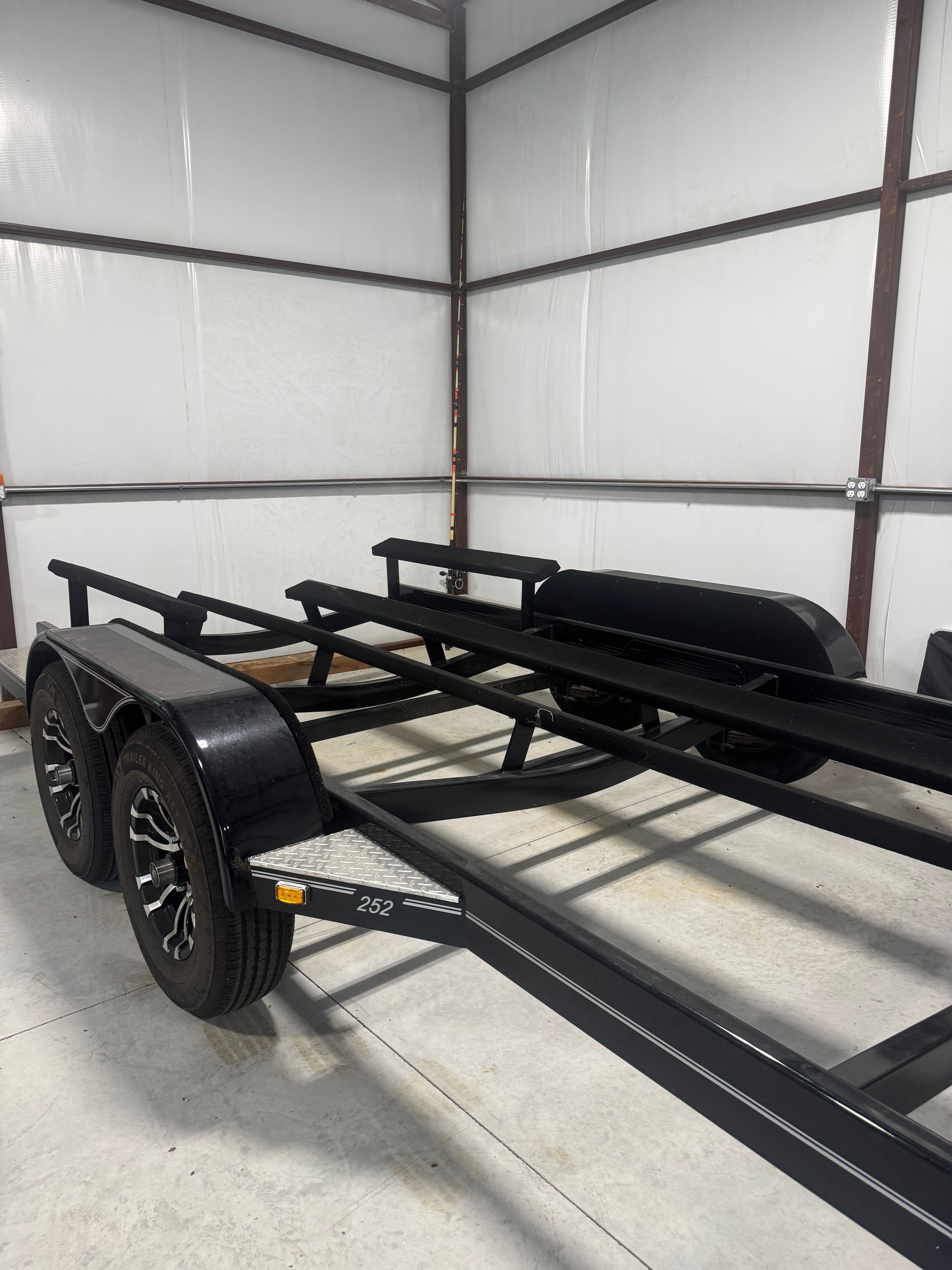 A black dual-axle boat trailer is parked in a storage area.