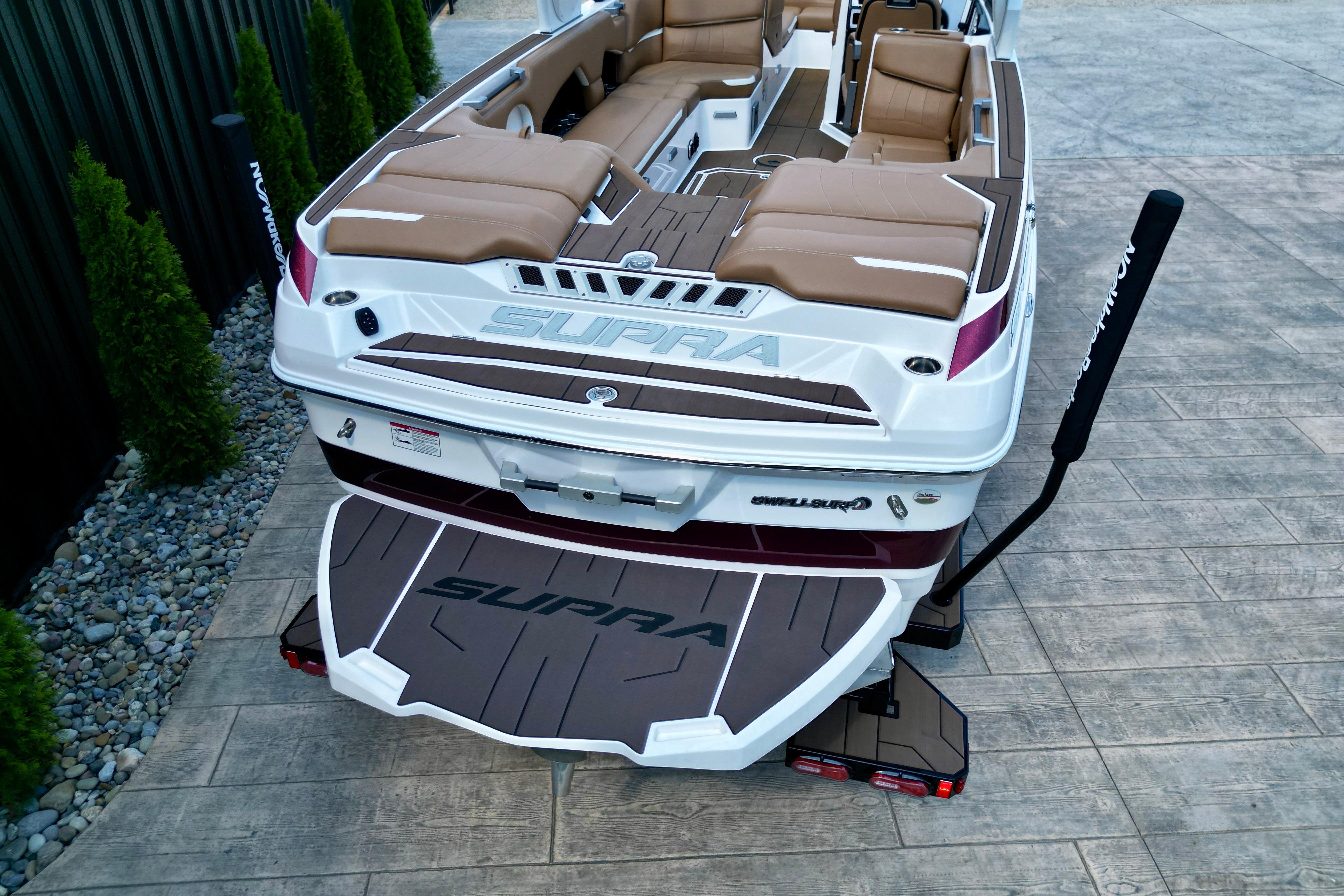 2021 Supra SE boat with tan seating and swim platform, parked on stone pavement.