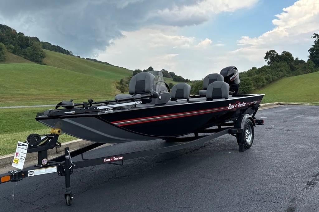 2026 Tracker Bass Tracker Classic XL boat on trailer, parked on asphalt near grassy hills.
