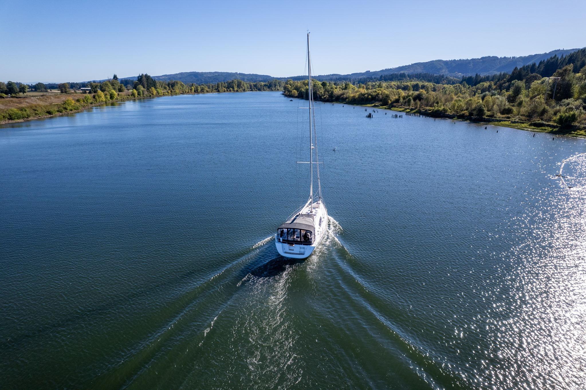 Sailboat Beneteau Oceanis 50 (2013) cruising on a scenic river under clear blue skies.