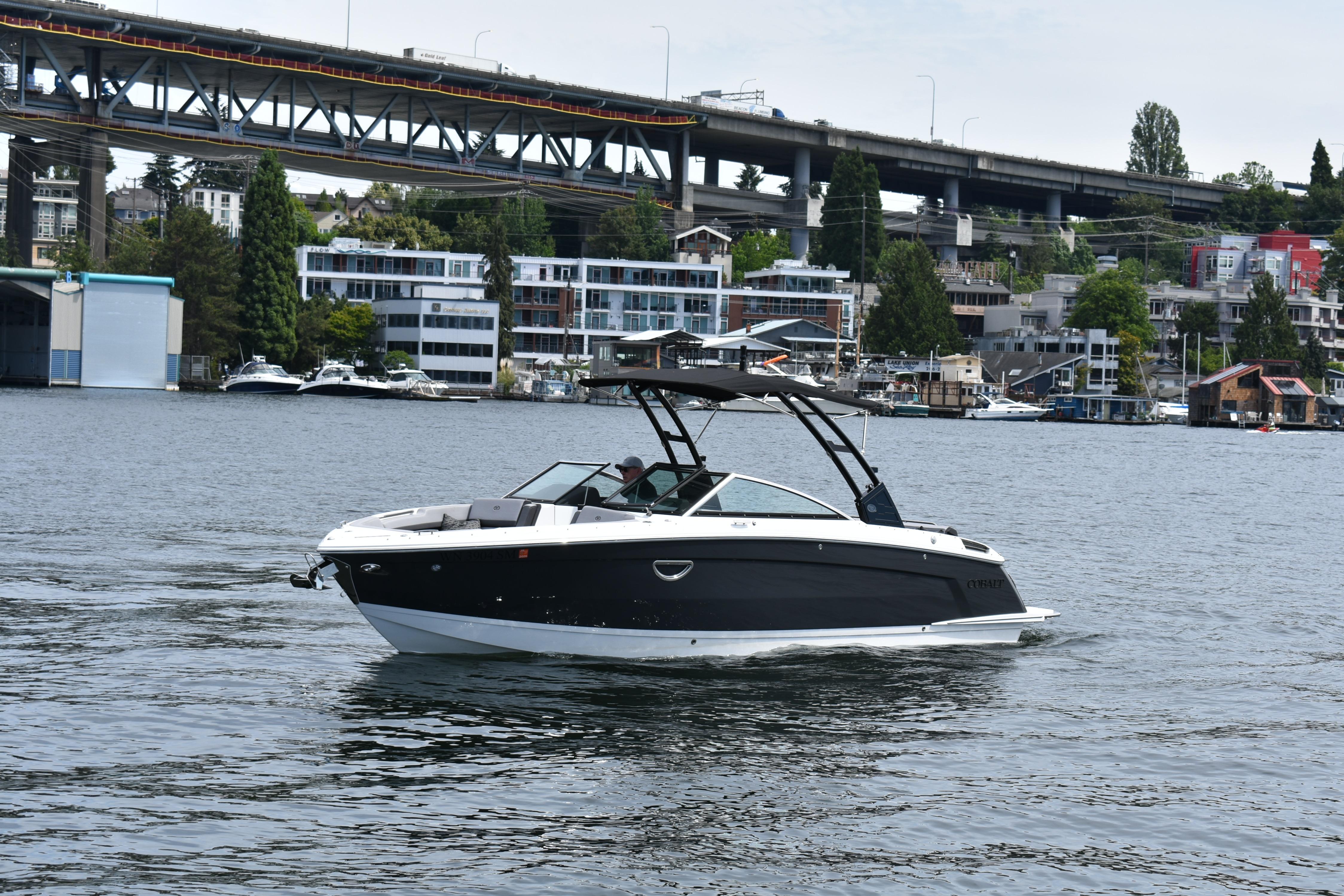 2023 Cobalt R8 boat cruising on a scenic urban waterway with bridge and buildings.