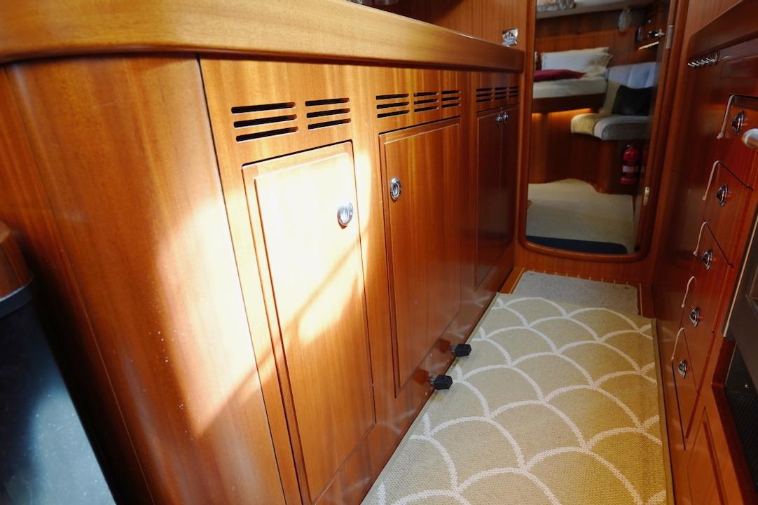 Luxurious wooden interior of 2015 Hallberg-Rassy 55 yacht, featuring elegant cabinetry and carpet.