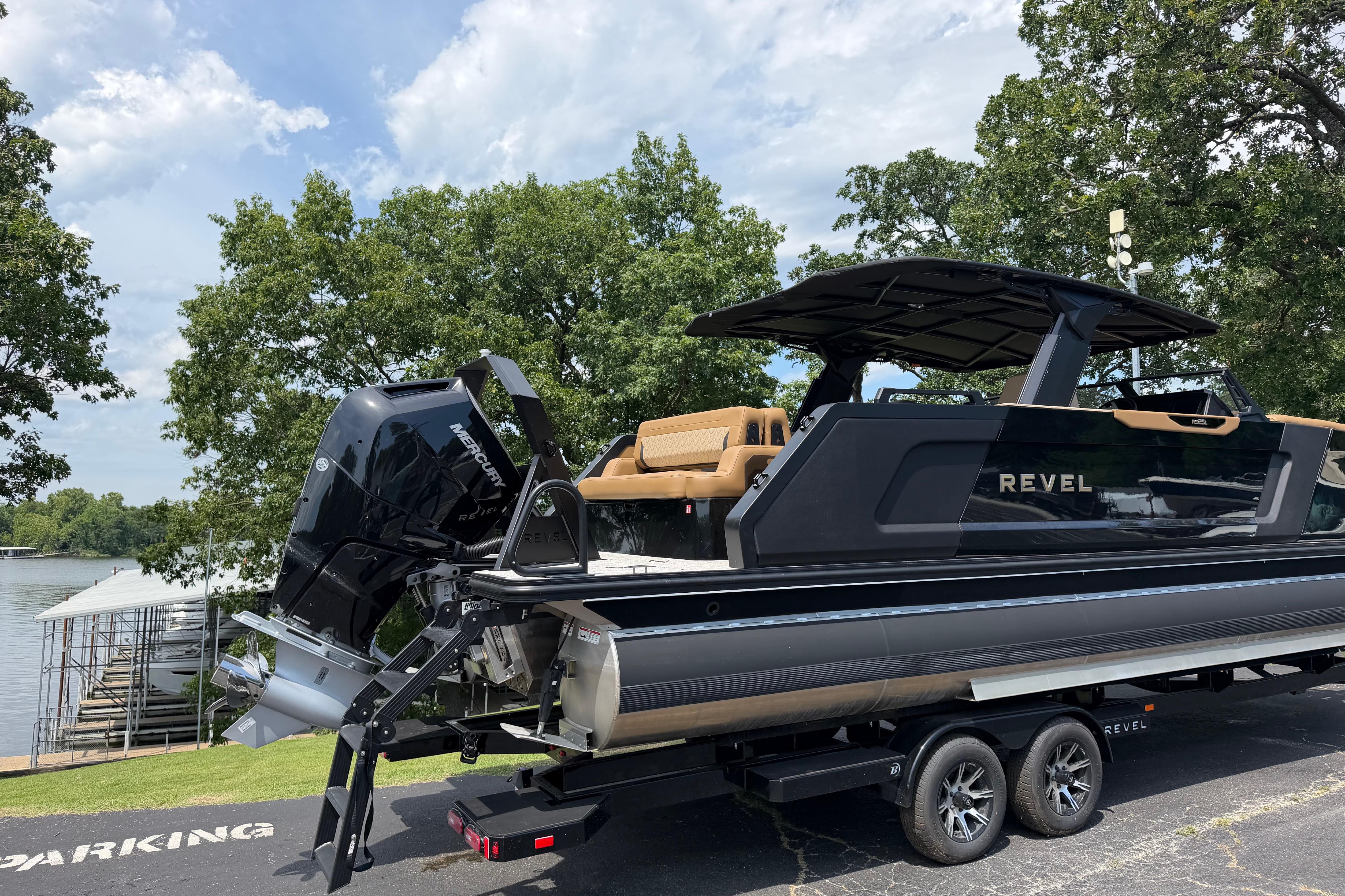 2026 Revel RS25L boat on trailer, parked near a lake with trees in the background.