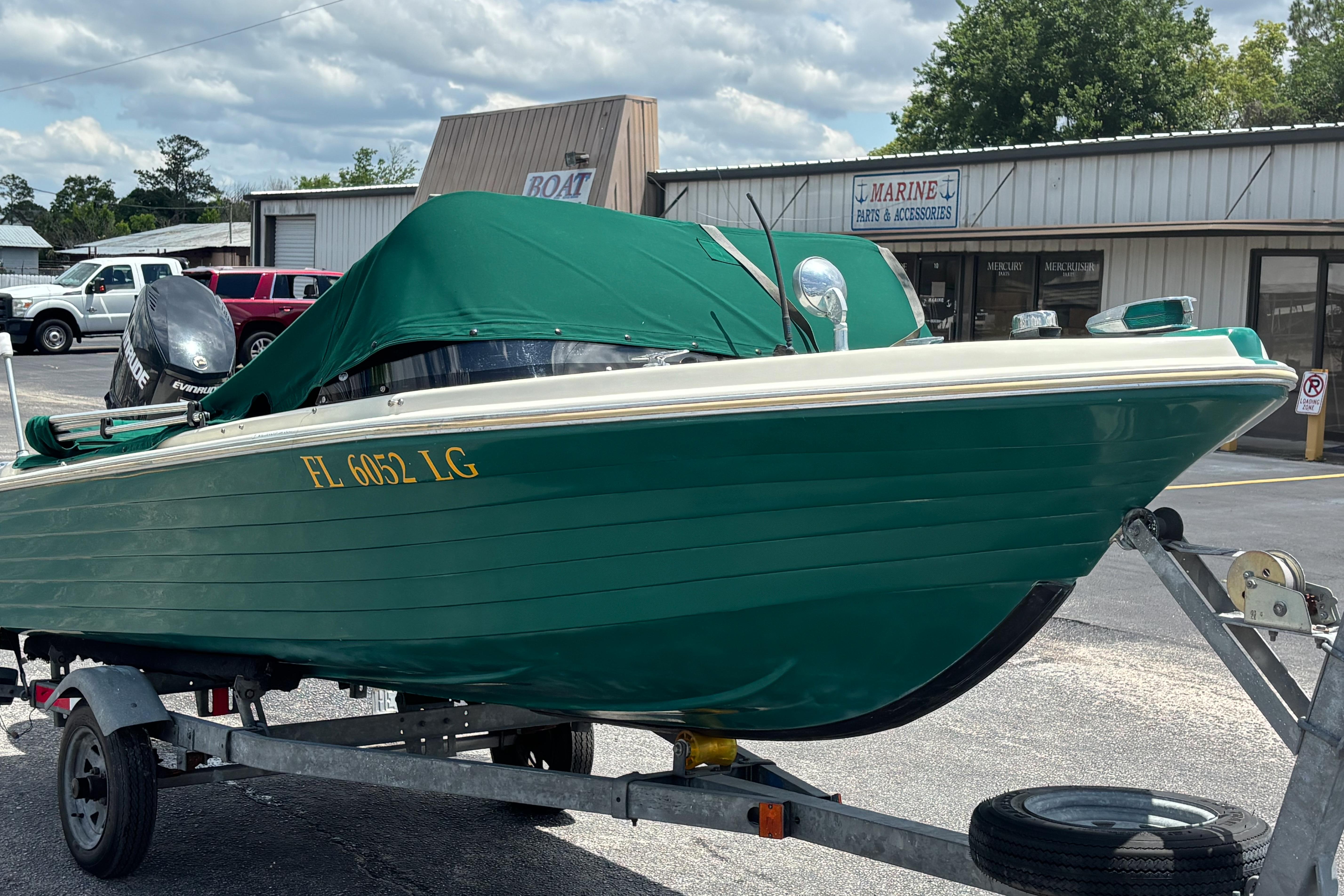 1966 Mohawk 15 boat with green cover on trailer, parked outside marine store.