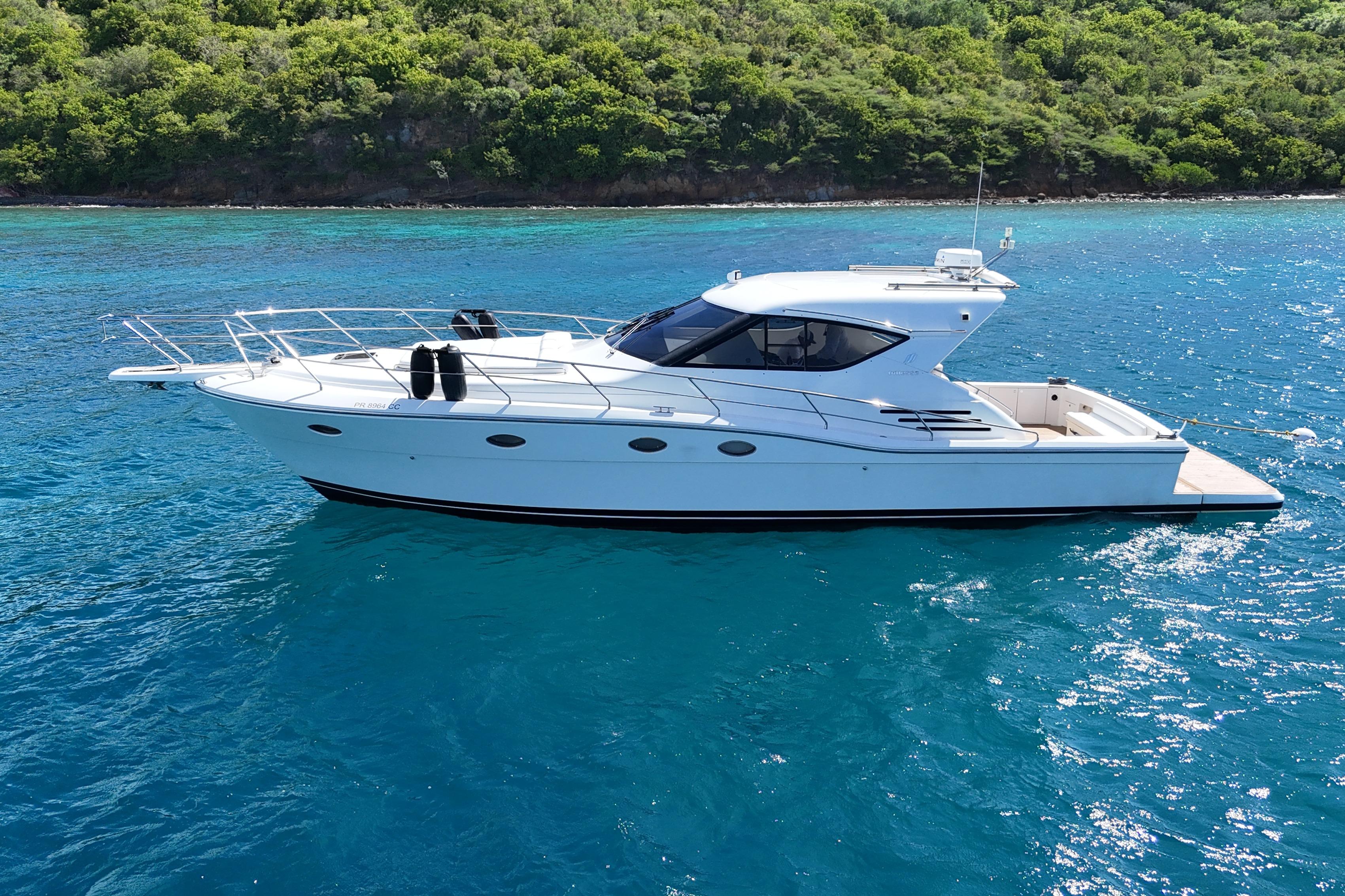2013 Uniesse 49 yacht cruising on clear blue waters near lush green coastline.