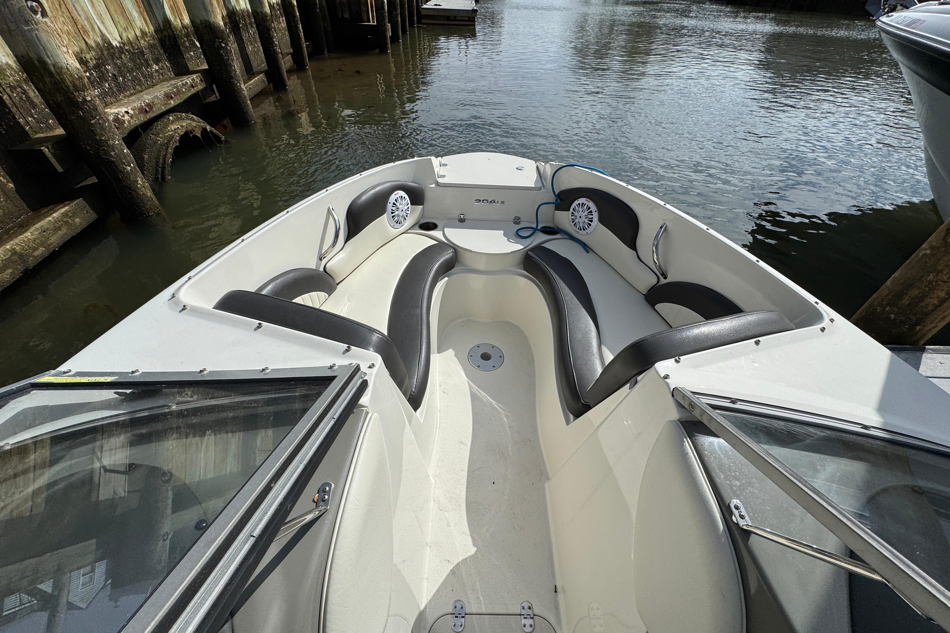 2019 Stingray 204 LR boat interior with black and white seating, docked by wooden pilings.
