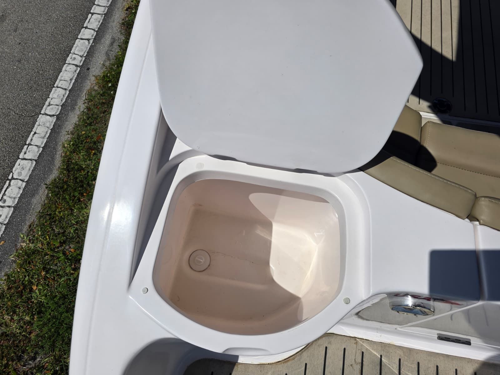 An open storage compartment on a boat with beige upholstery and wooden flooring.