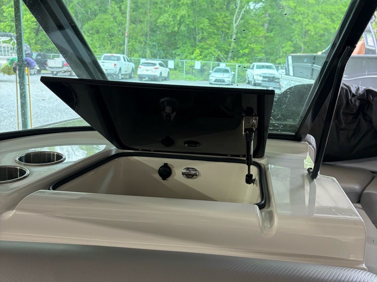An open storage compartment on a boat with cup holders beside it.