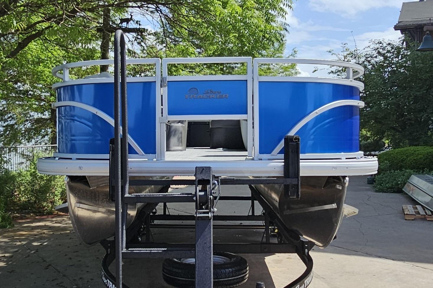 2026 Sun Tracker Fishin' Barge 20 DLX pontoon boat on trailer, surrounded by greenery.