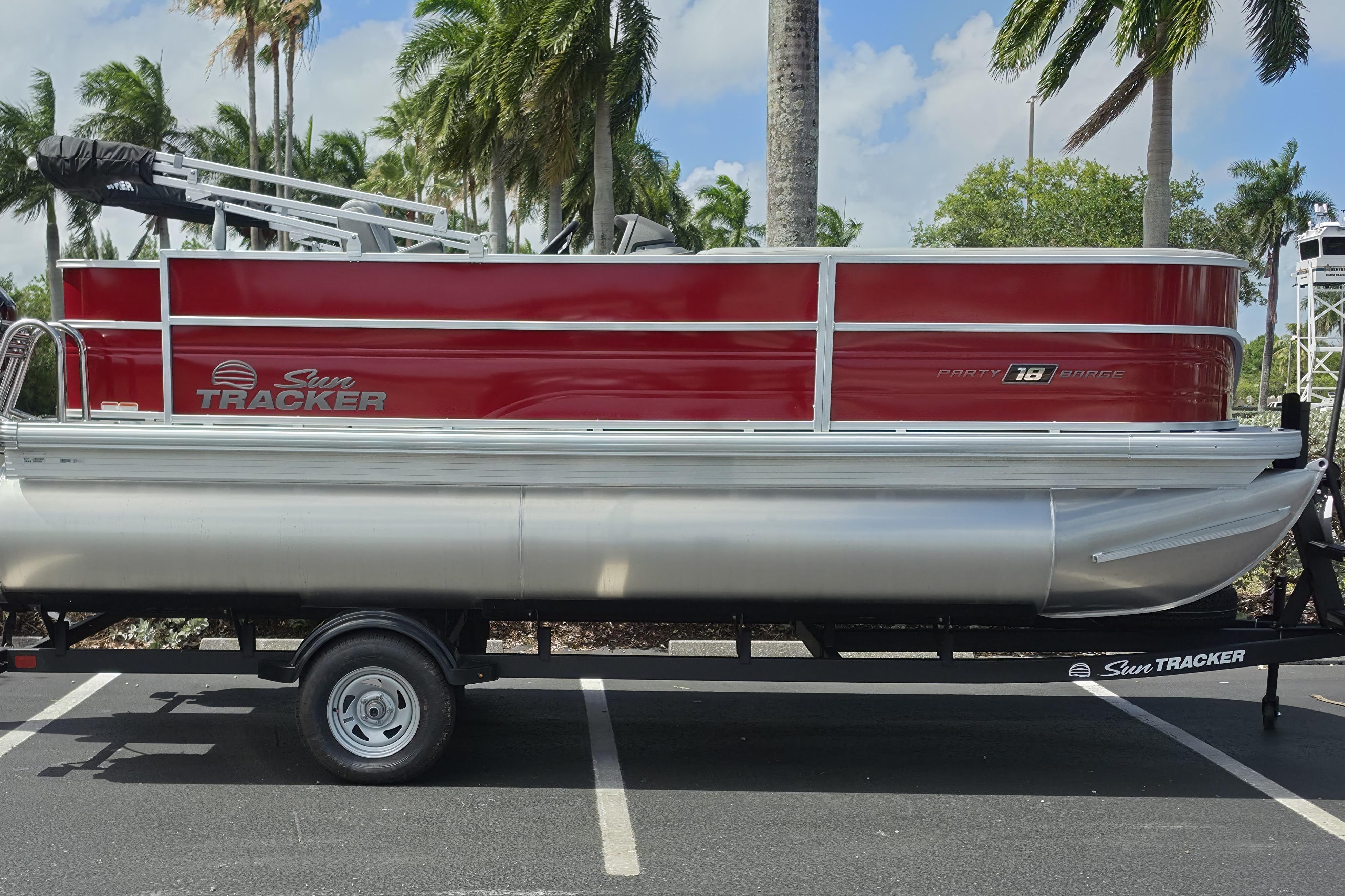 2026 Sun Tracker Party Barge 18 DLX pontoon boat on trailer, parked with palm trees.