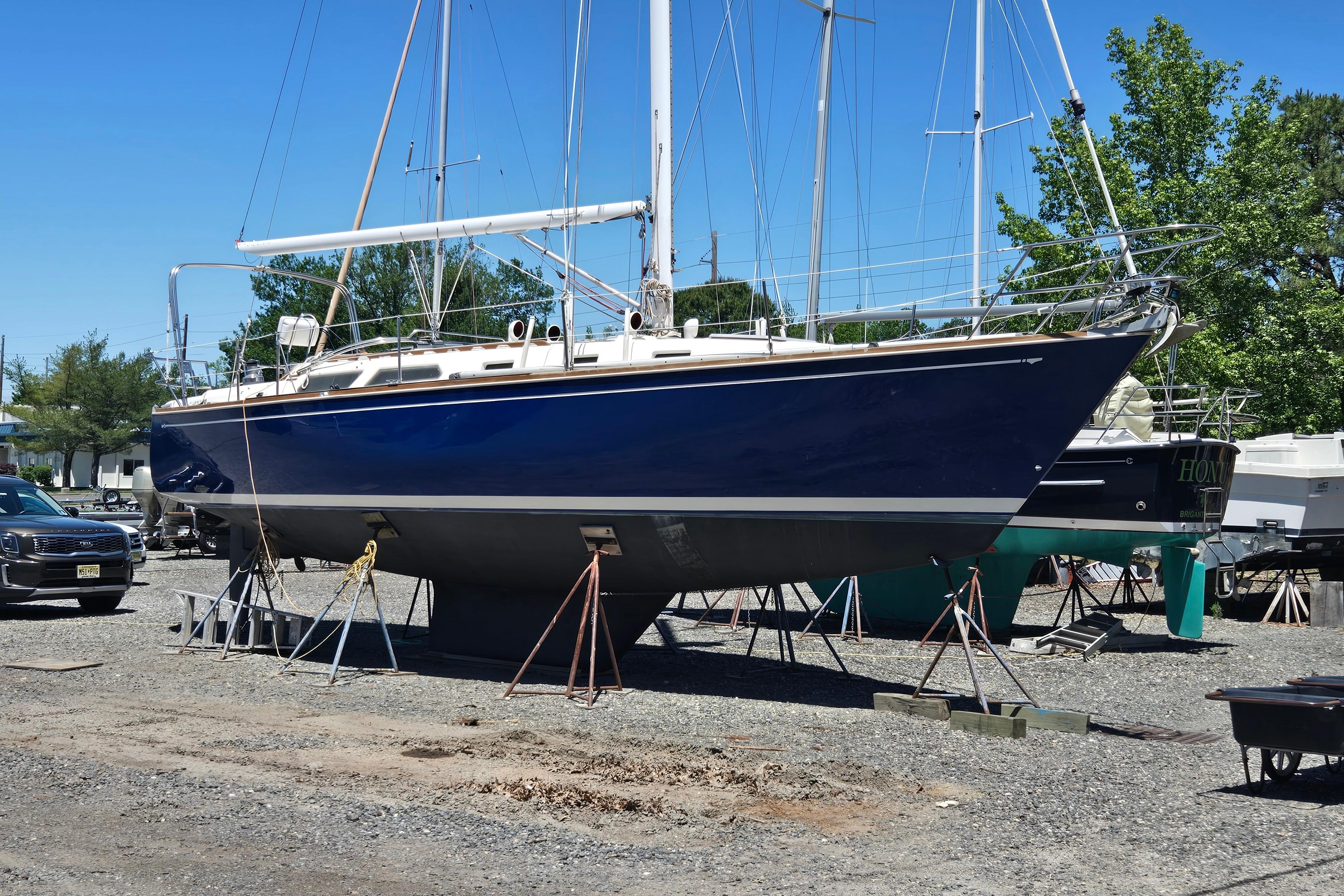 1988 Sabre 38 sailboat on stands in a boatyard under clear blue sky.