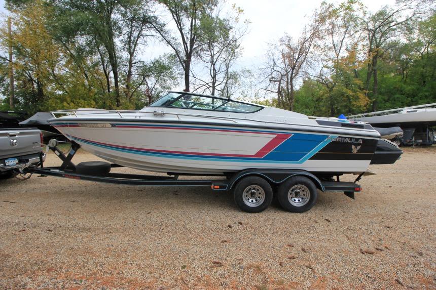 1989 Formula 223 SS boat on trailer, parked outdoors with trees in background.