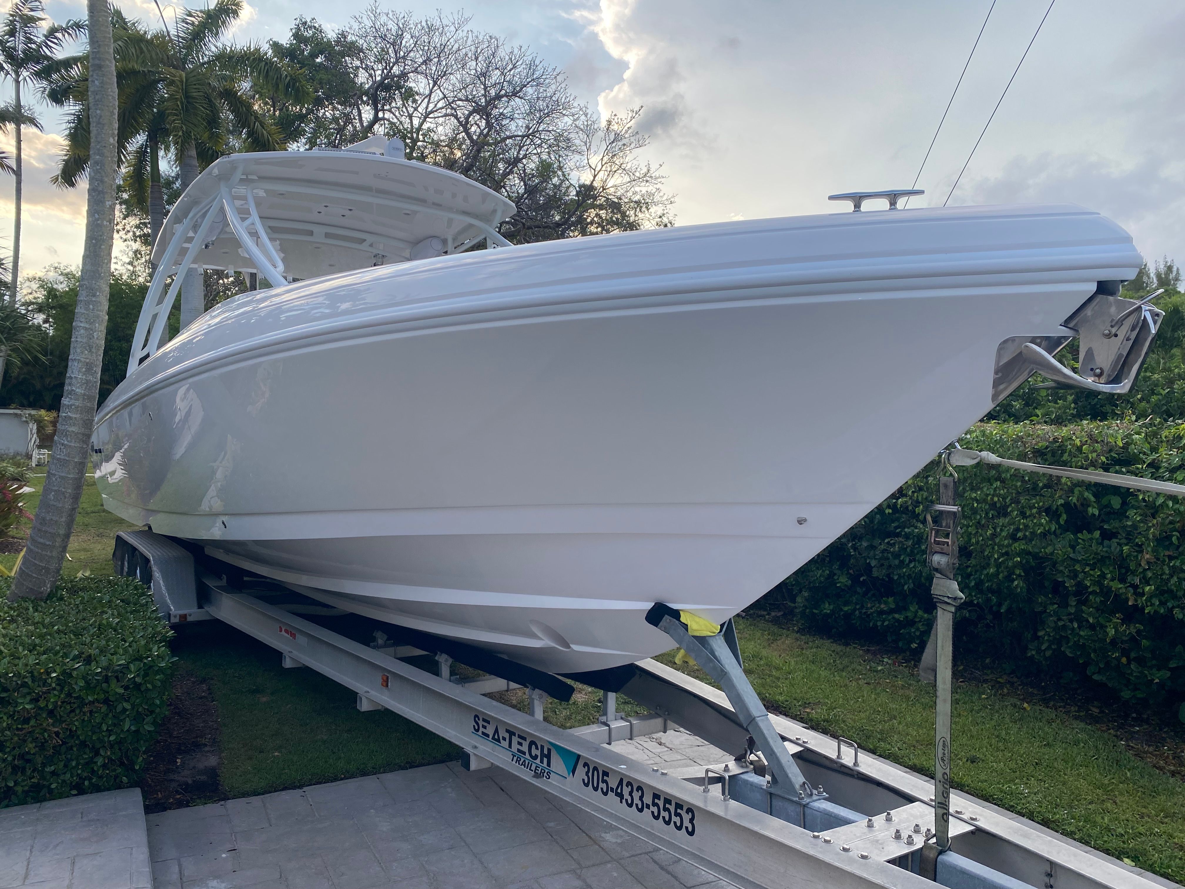 A white 2011 Intrepid 37 boat on a trailer, surrounded by palm trees and bushes.