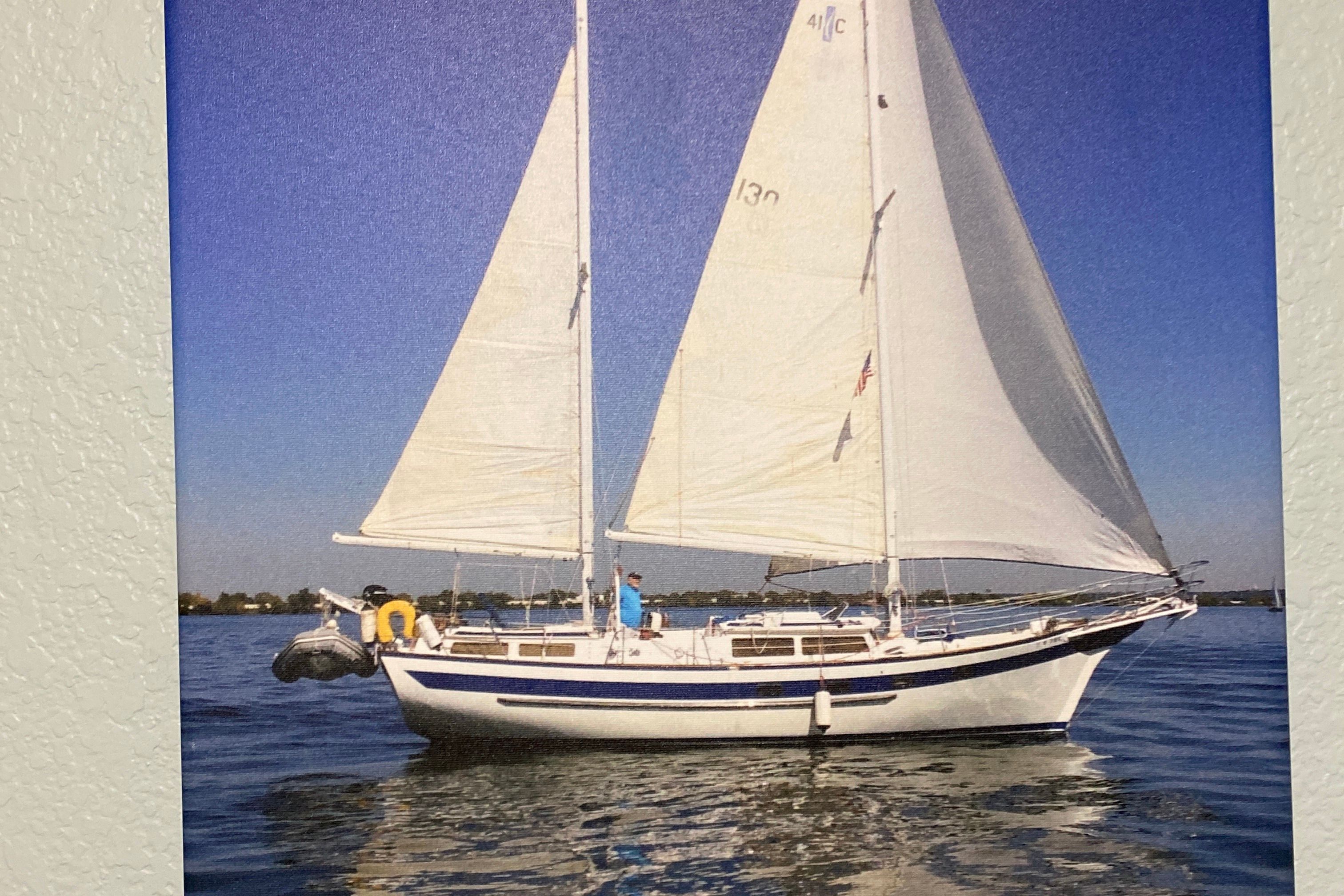 A 1983 Islander Freeport sailboat glides on calm water under a clear blue sky.