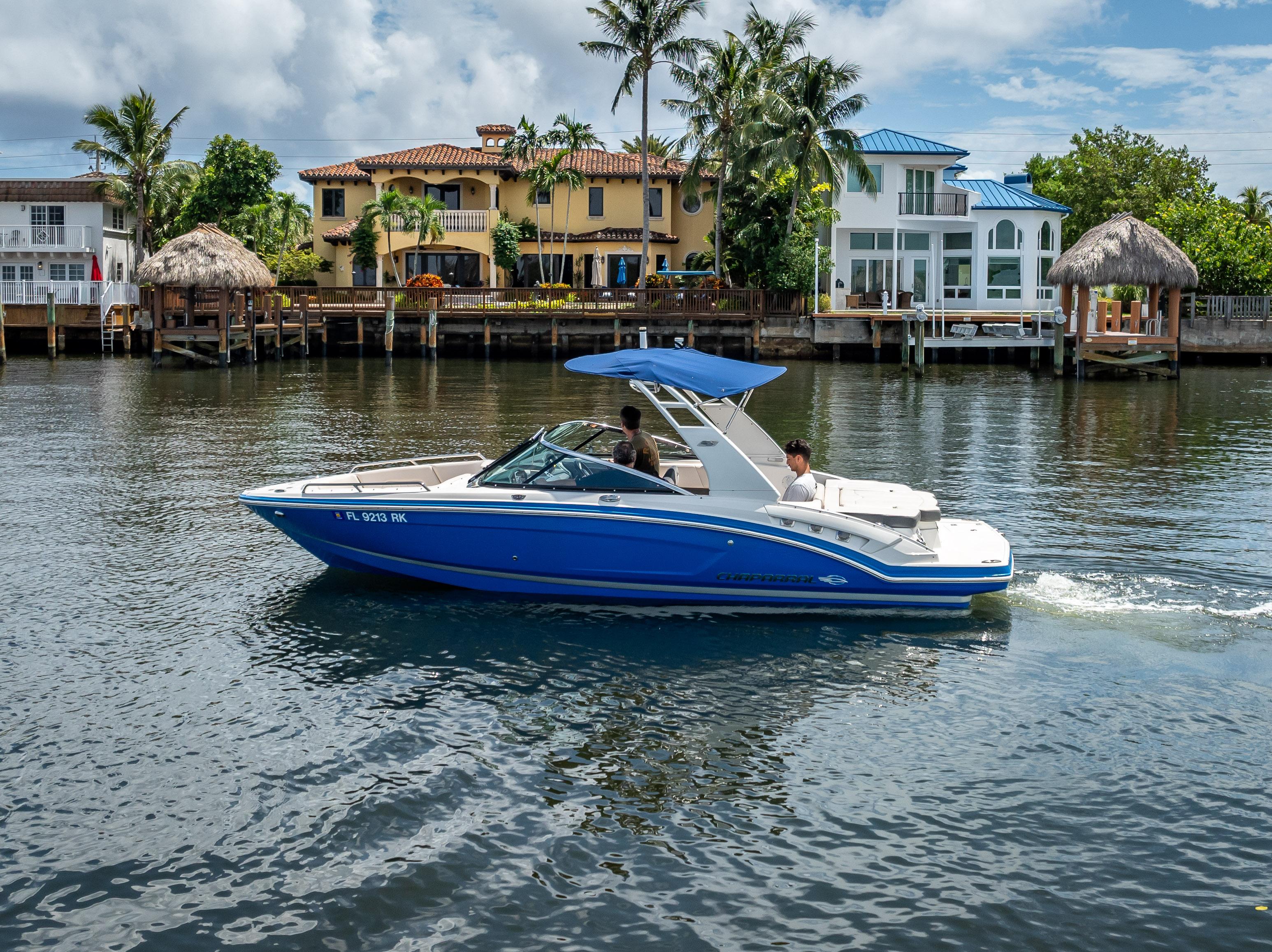2017 Chaparral 227 SSX boat cruising on a scenic waterfront with luxury homes.
