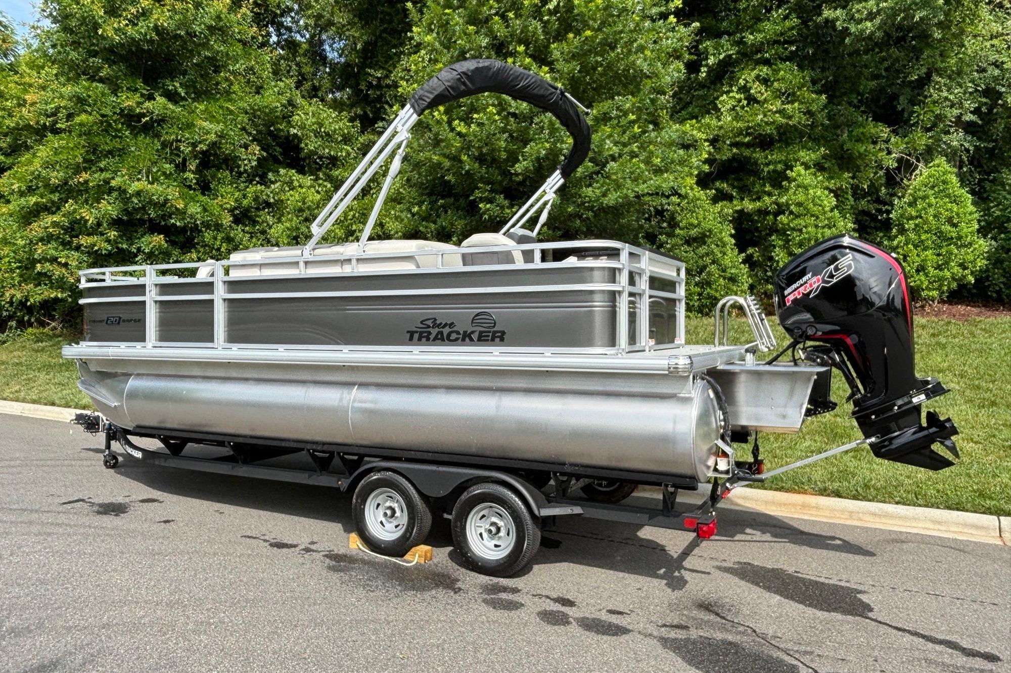 2026 Sun Tracker Fishin' Barge 20 DLX pontoon boat on trailer, parked outdoors.