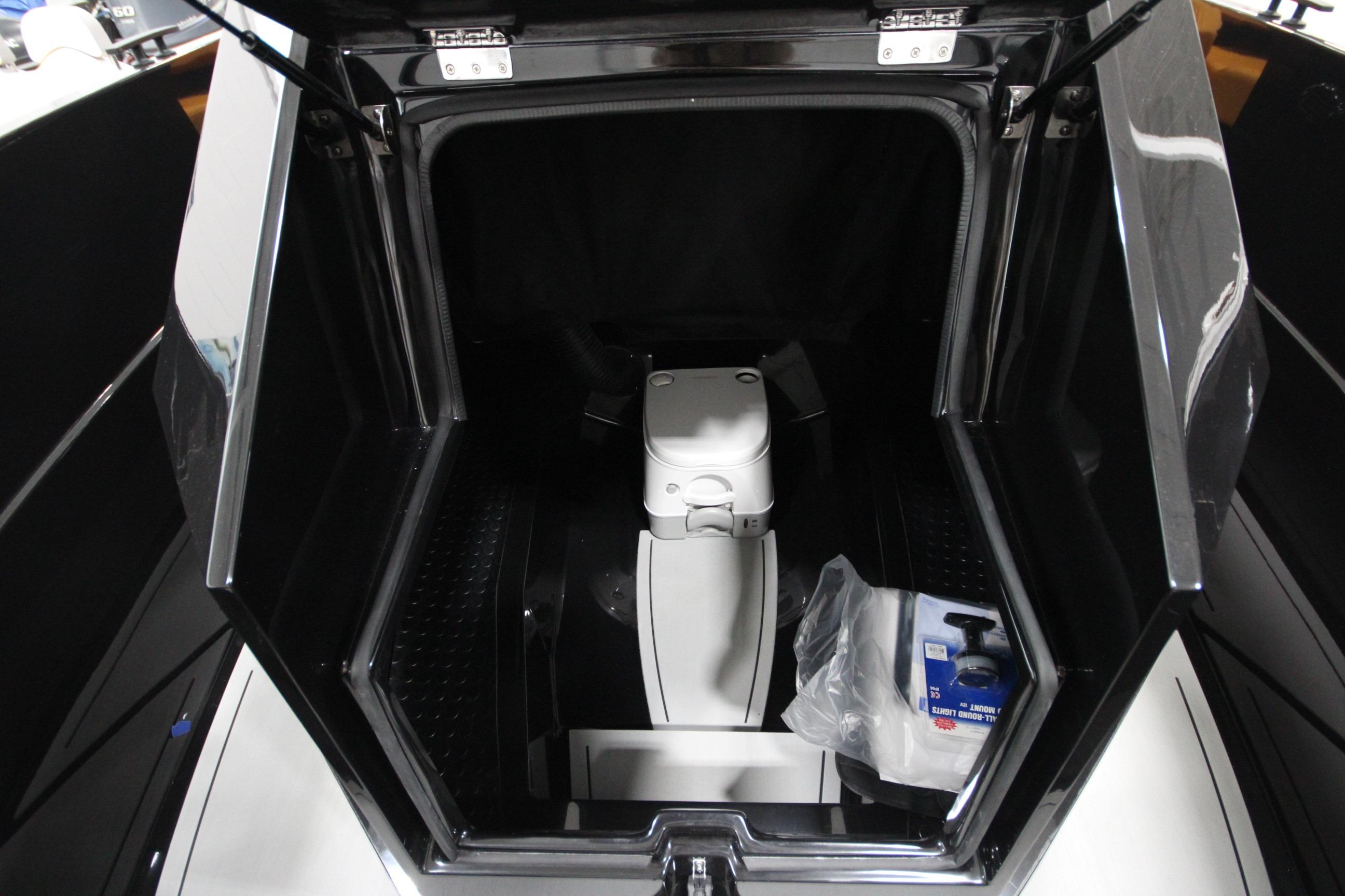 Open storage compartment of Iron 767 boat, featuring a portable toilet and cleaning supplies.