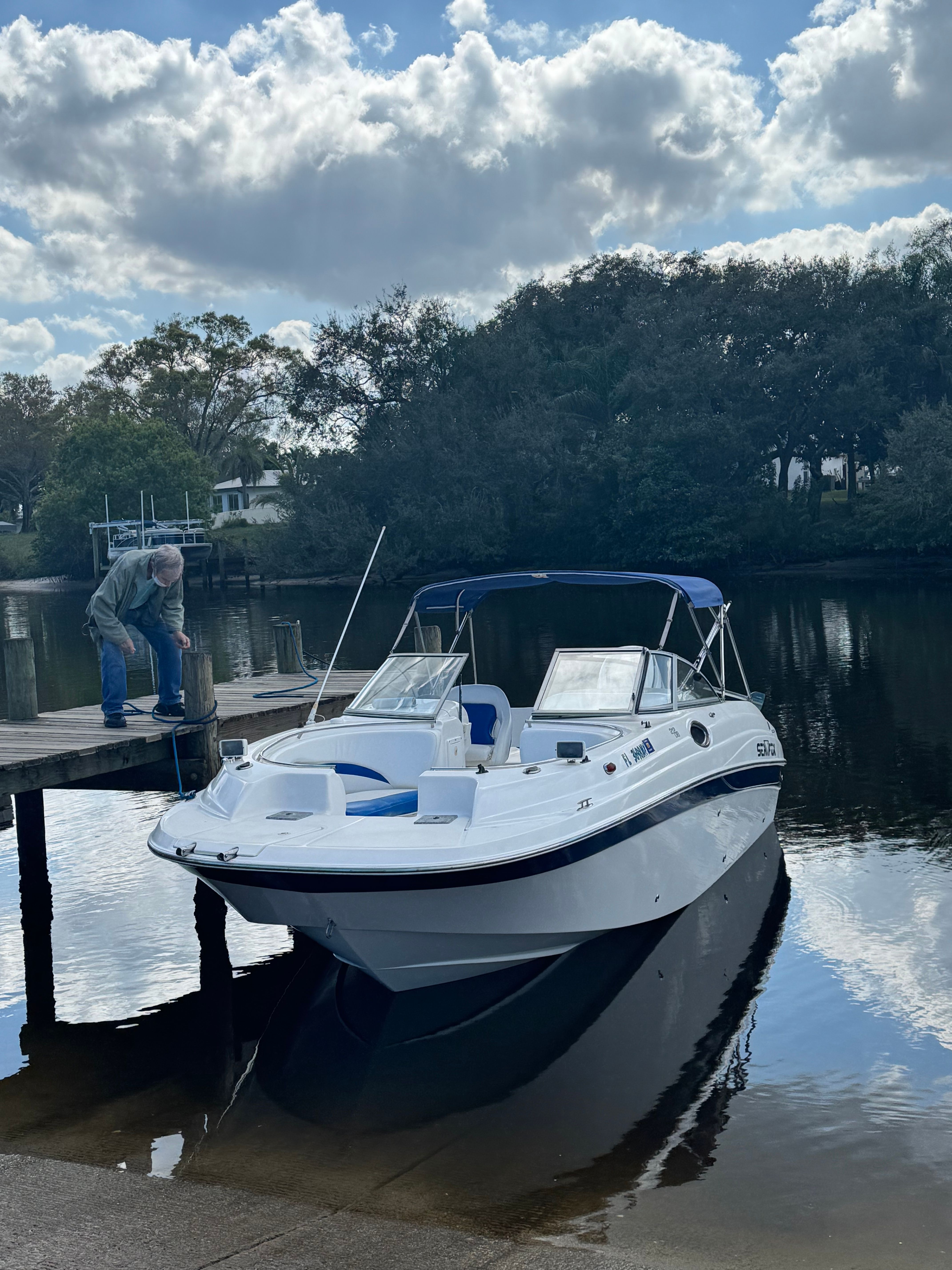 A white motorboat is docked at a wooden pier. A man stands on the pier.