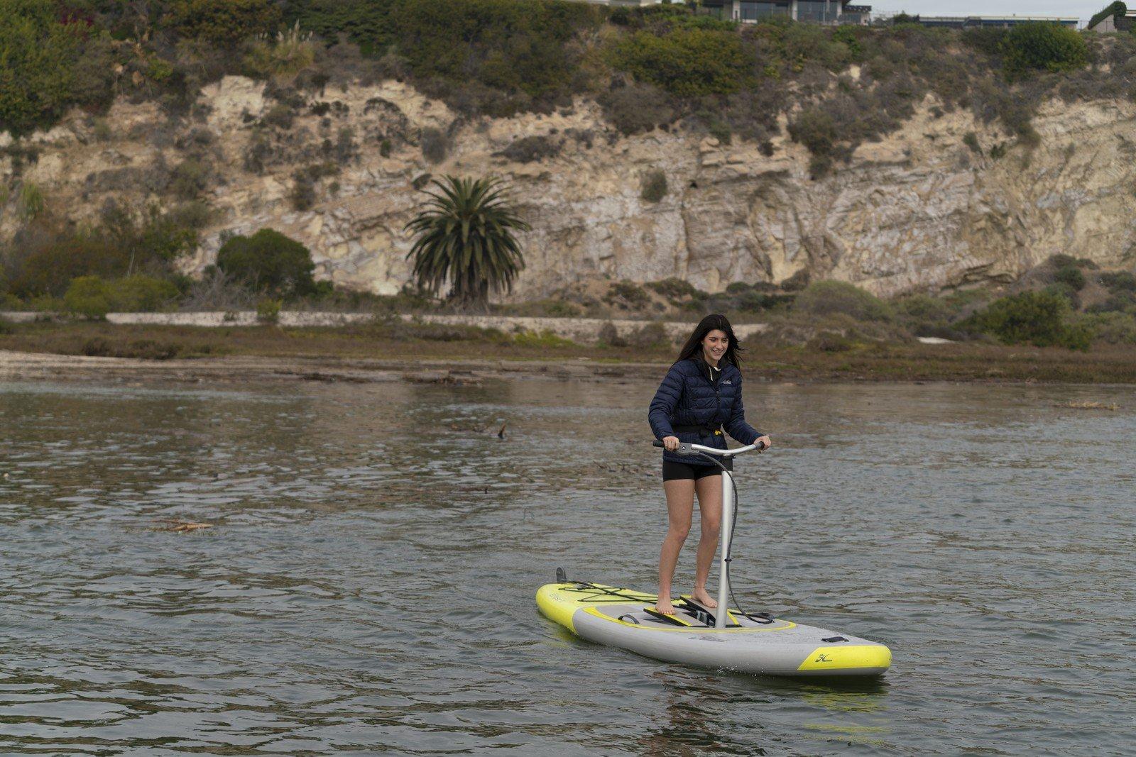 Woman enjoying a ride on a 2025 Hobie iEclipse pedalboard in a scenic waterway.