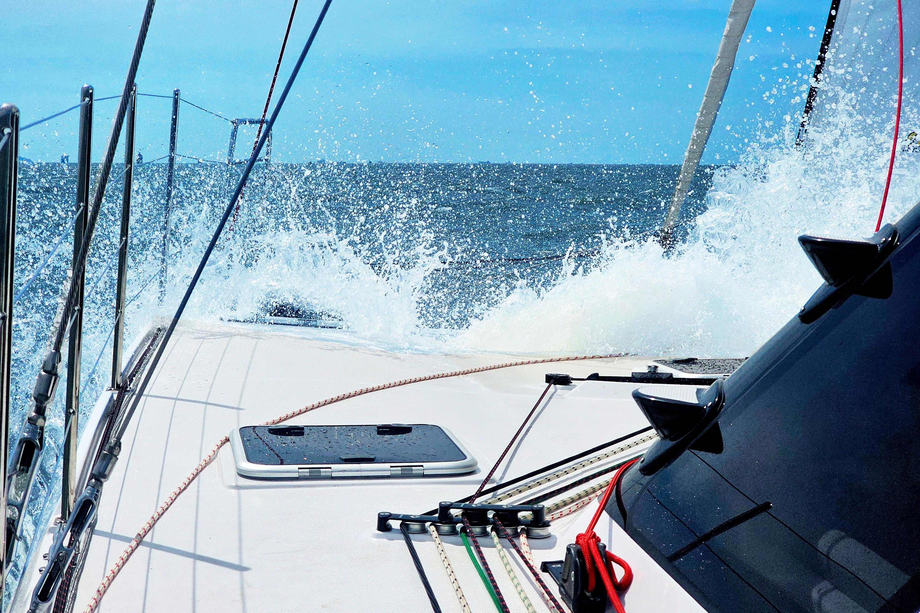 Sailing on a 2026 Seawind 1160XL catamaran, waves splashing on deck under clear blue skies.
