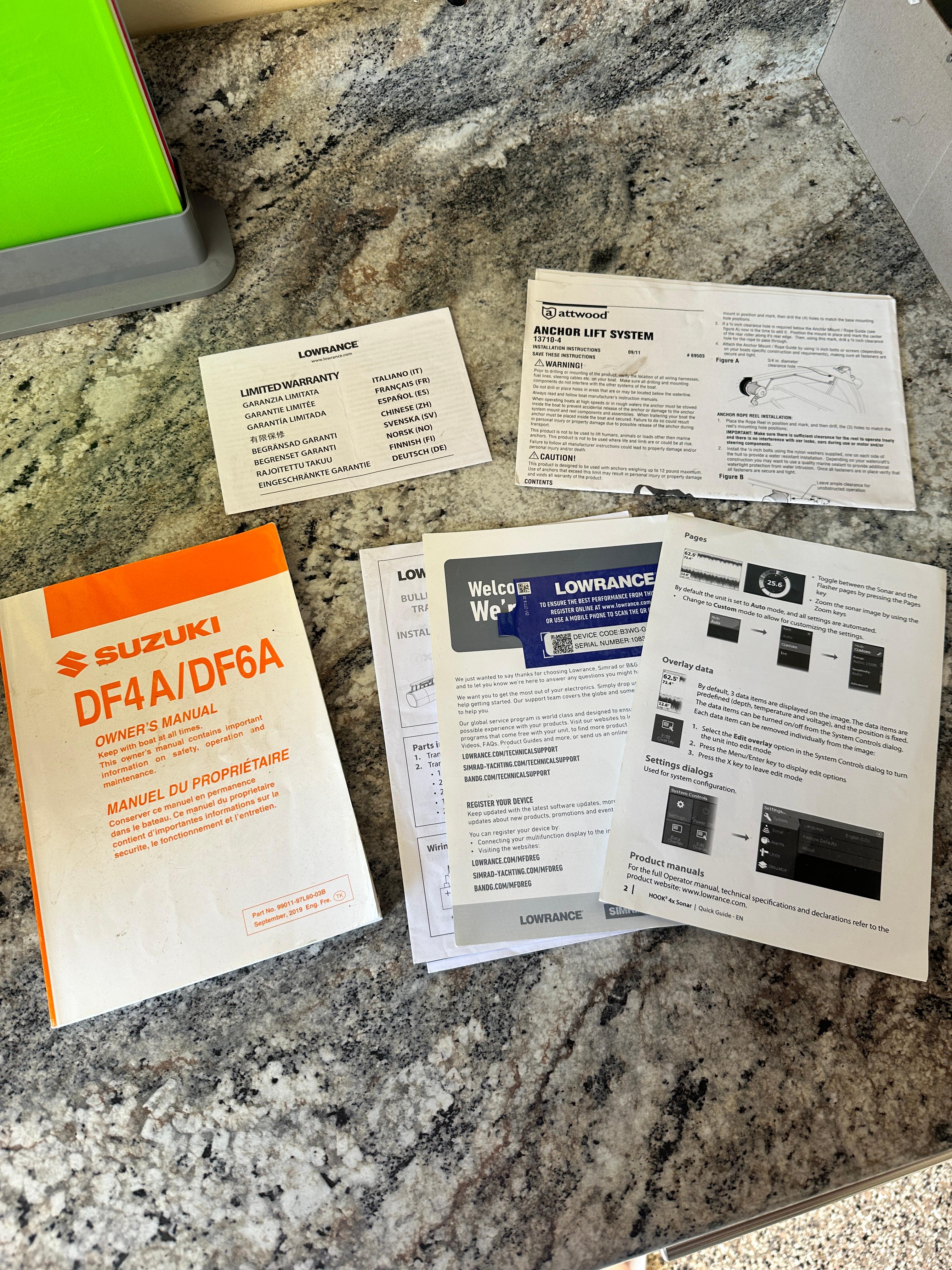 Assorted manuals and documents on a granite surface, including Suzuki DF4A/DF6A owner's manual.
