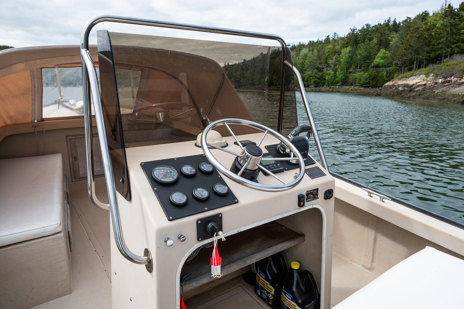 1989 Ellis 24 Open boat cockpit with steering wheel, gauges, and scenic water view.
