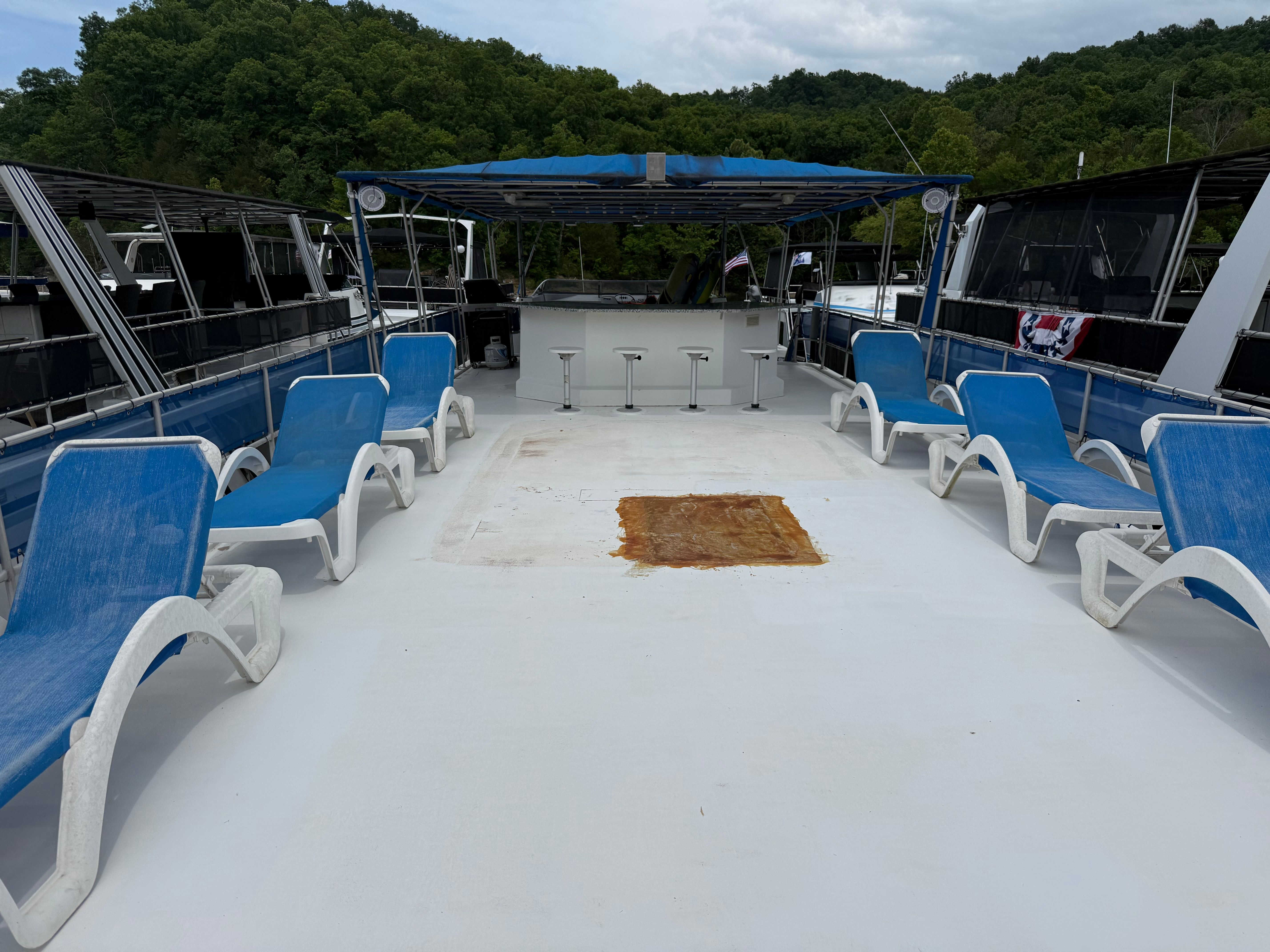 The deck of a houseboat with blue lounge chairs and a bar under a blue canopy.