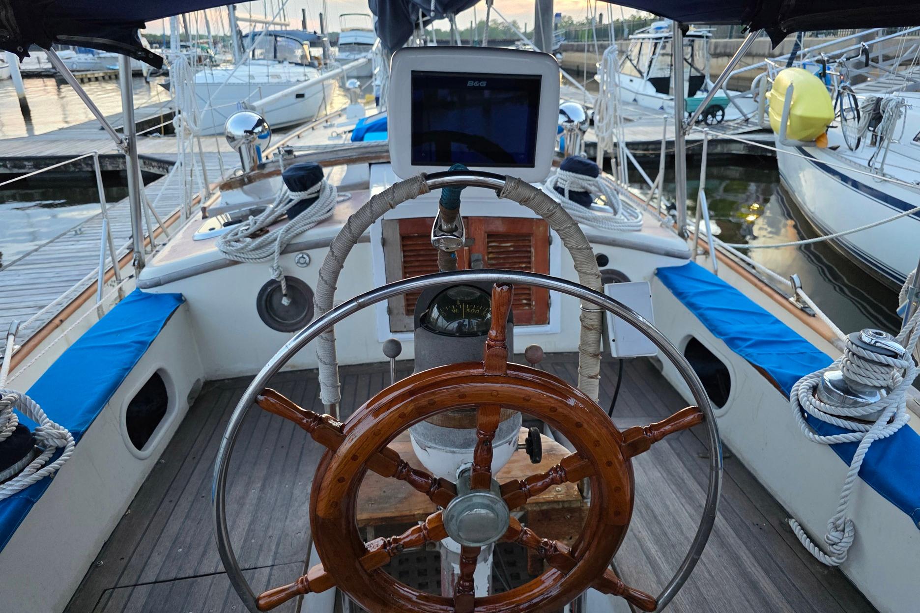 Cockpit of a 1982 Tayana 37 sailboat with wooden steering wheel and navigation equipment.
