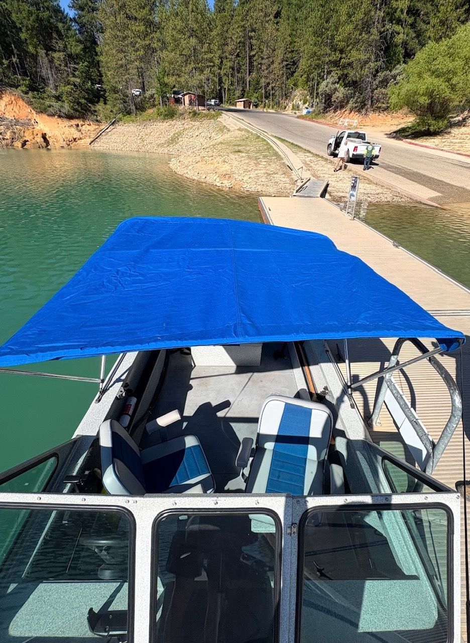 A 2002 Stryker Rogue boat with a blue canopy docked at a lakeside pier.