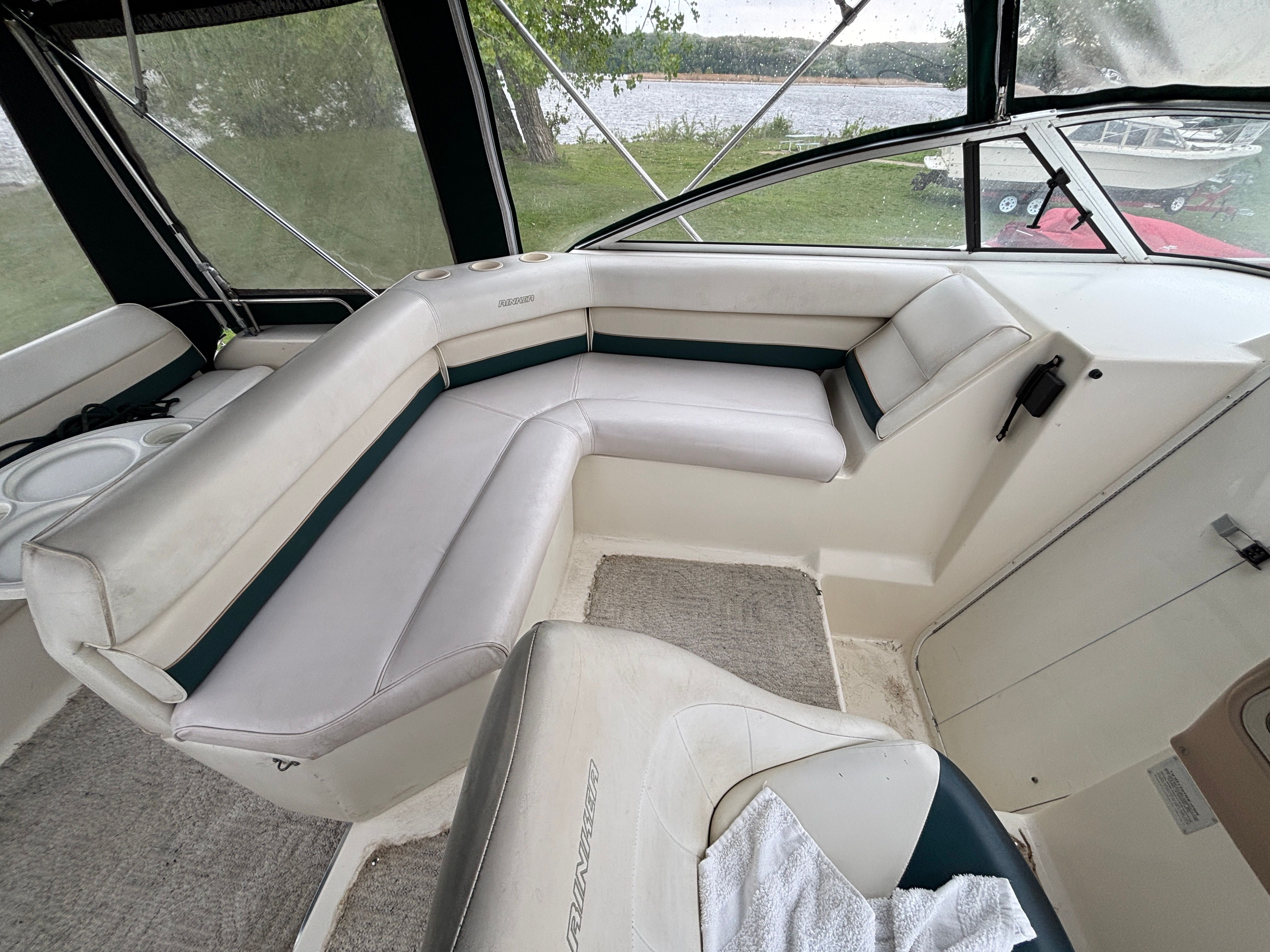Interior of a boat with white and green seating, carpeted floor, and windows overlooking water.