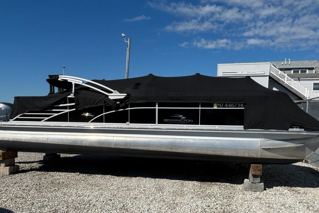 2014 Bennington 2575 RCW pontoon boat covered, parked on gravel under a clear blue sky.