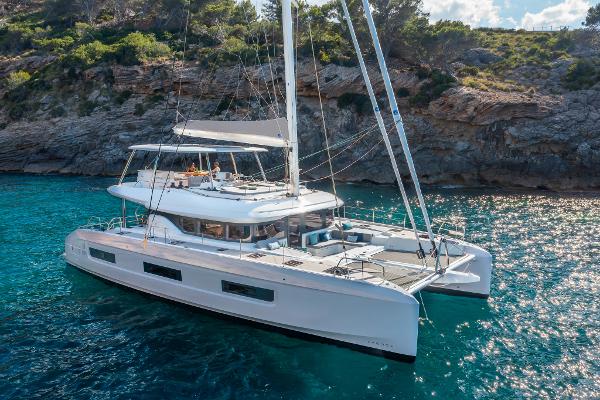 2025 Lagoon 60 catamaran sailing near rocky coastline in clear blue waters.