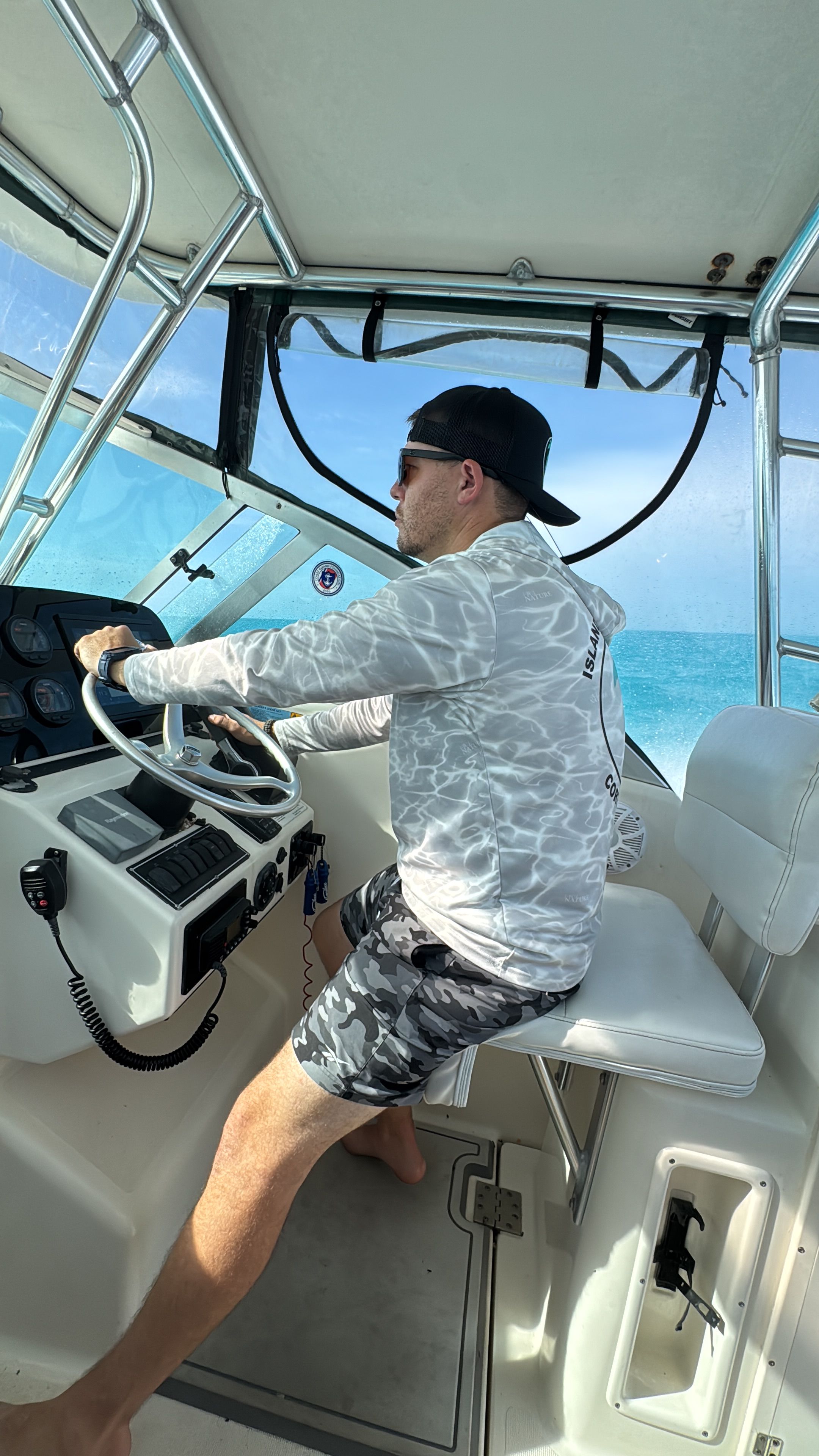 A man is steering a boat with a white helm and blue ocean backdrop.