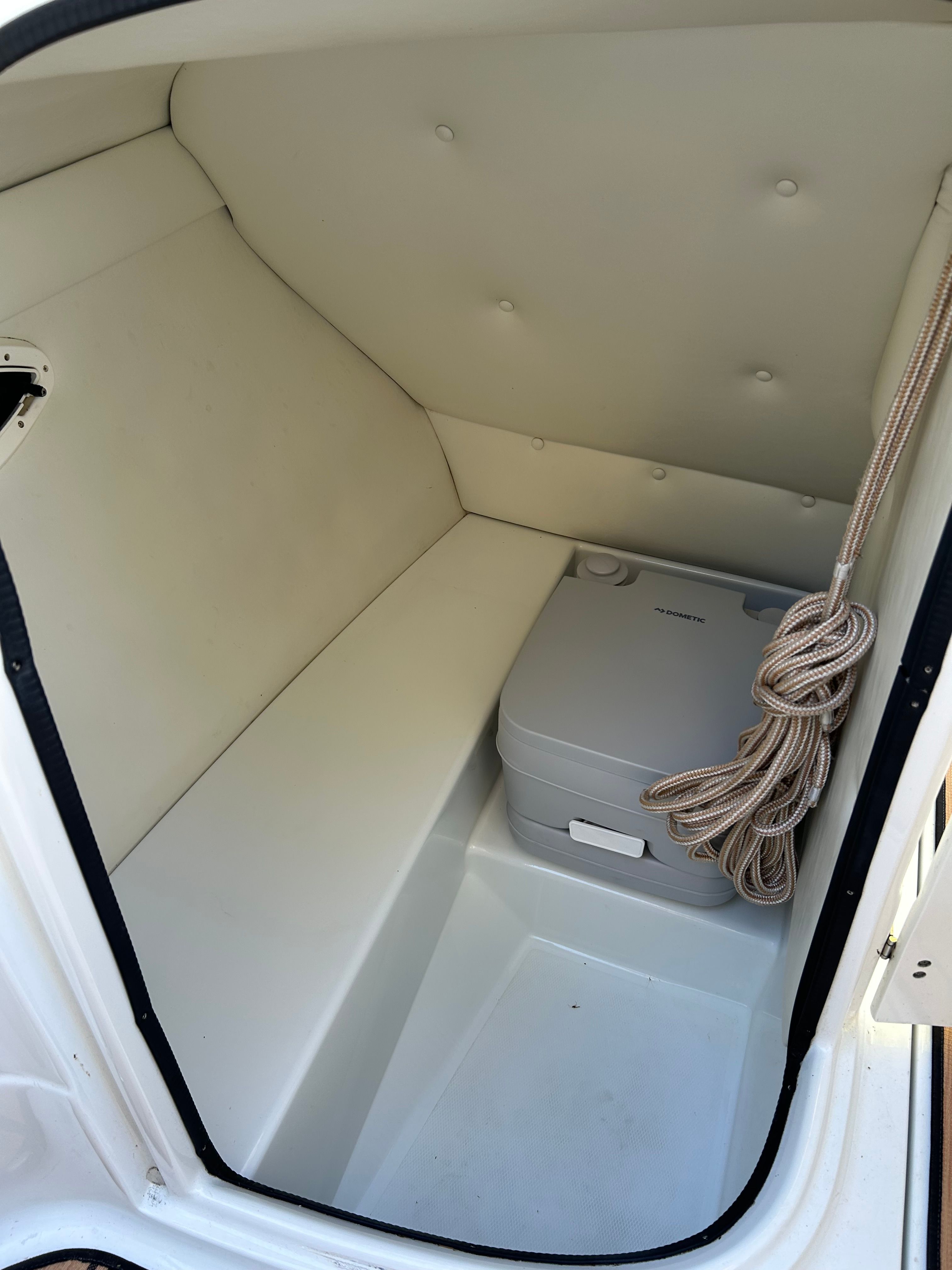The image shows a small cabin with a portable toilet and a rope on the wall.