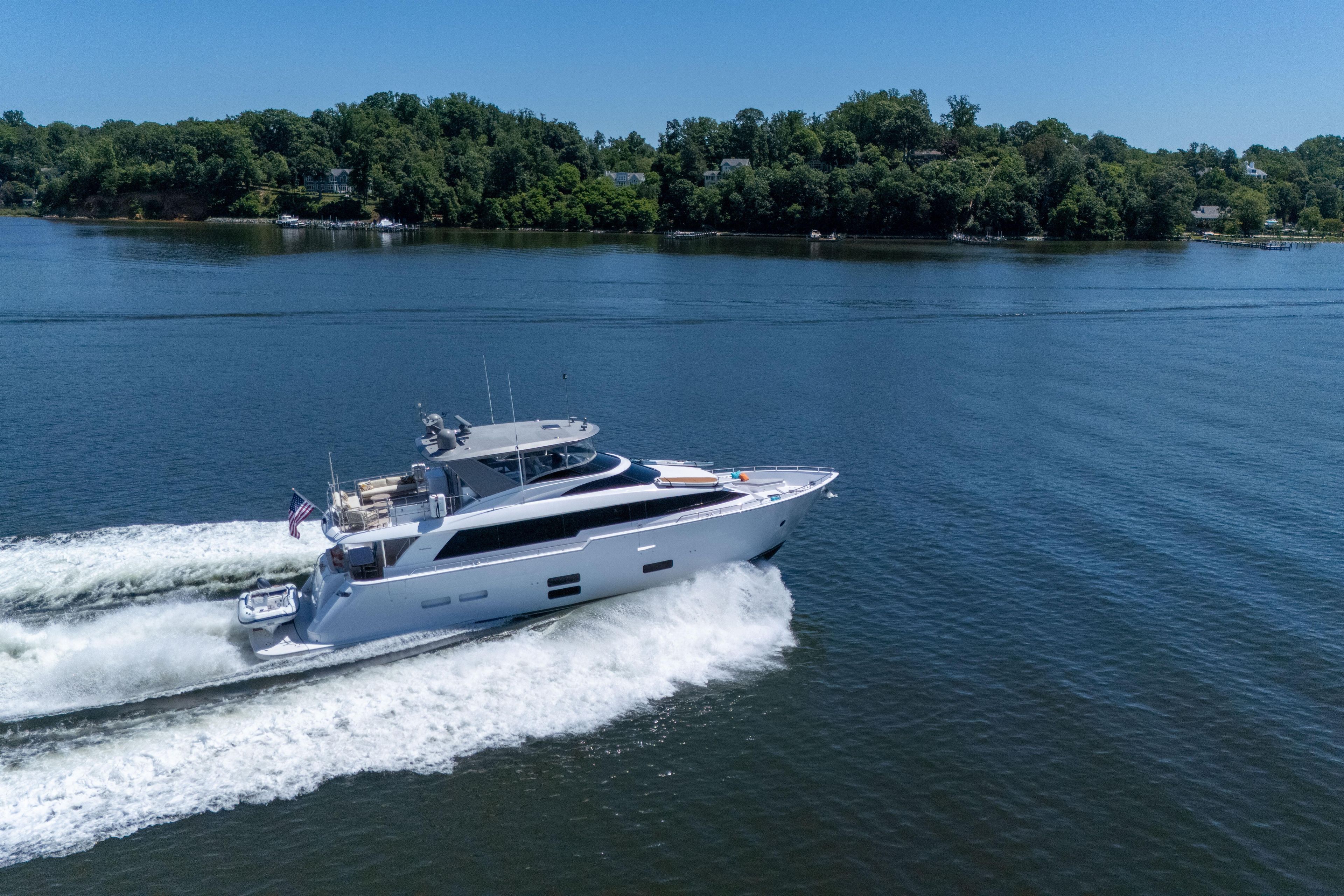 2021 Hatteras M75 Panacera yacht cruising on a serene lake with lush green shoreline.