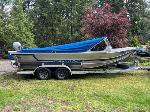 1986 Custom Jet Boat with blue cover on trailer in a green setting.
