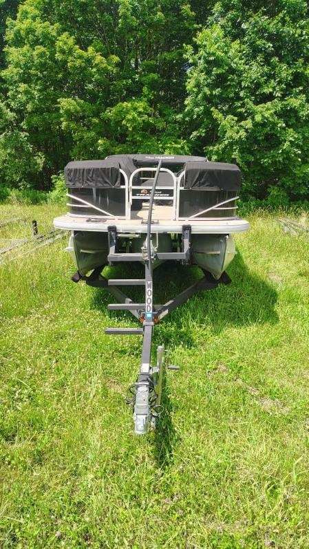 A 2019 White River sf22xp3 pb bk pontoon boat on a trailer in a grassy area.