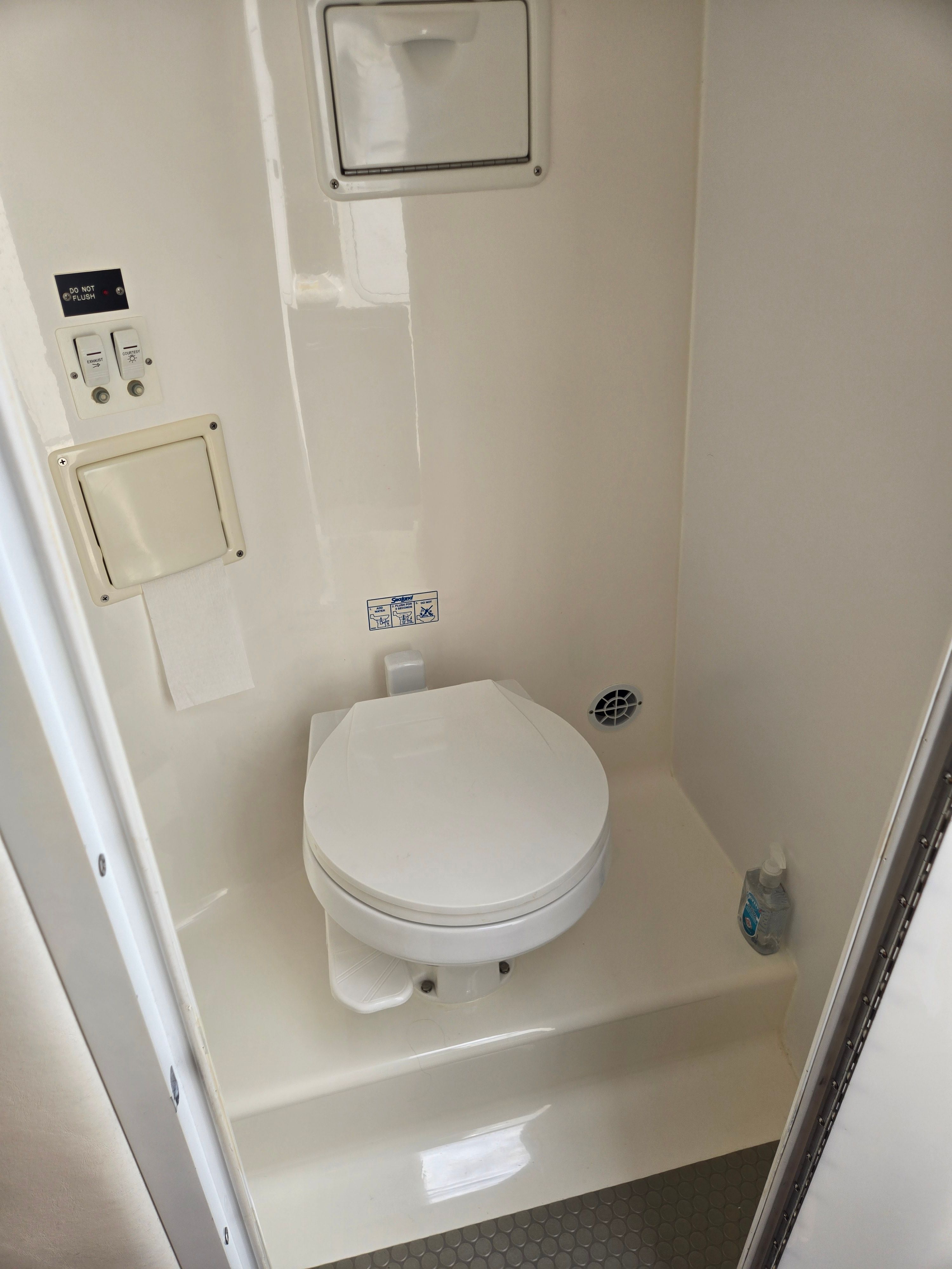 A clean, compact bathroom with a toilet and a small ventilation grate.