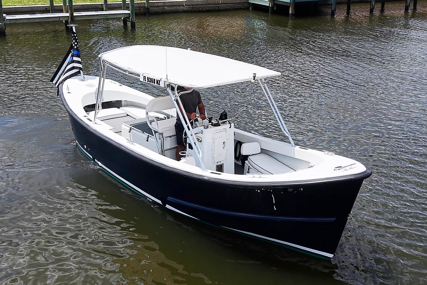 Custom 1969 boat with canopy cruising on a calm waterway, displaying a flag.