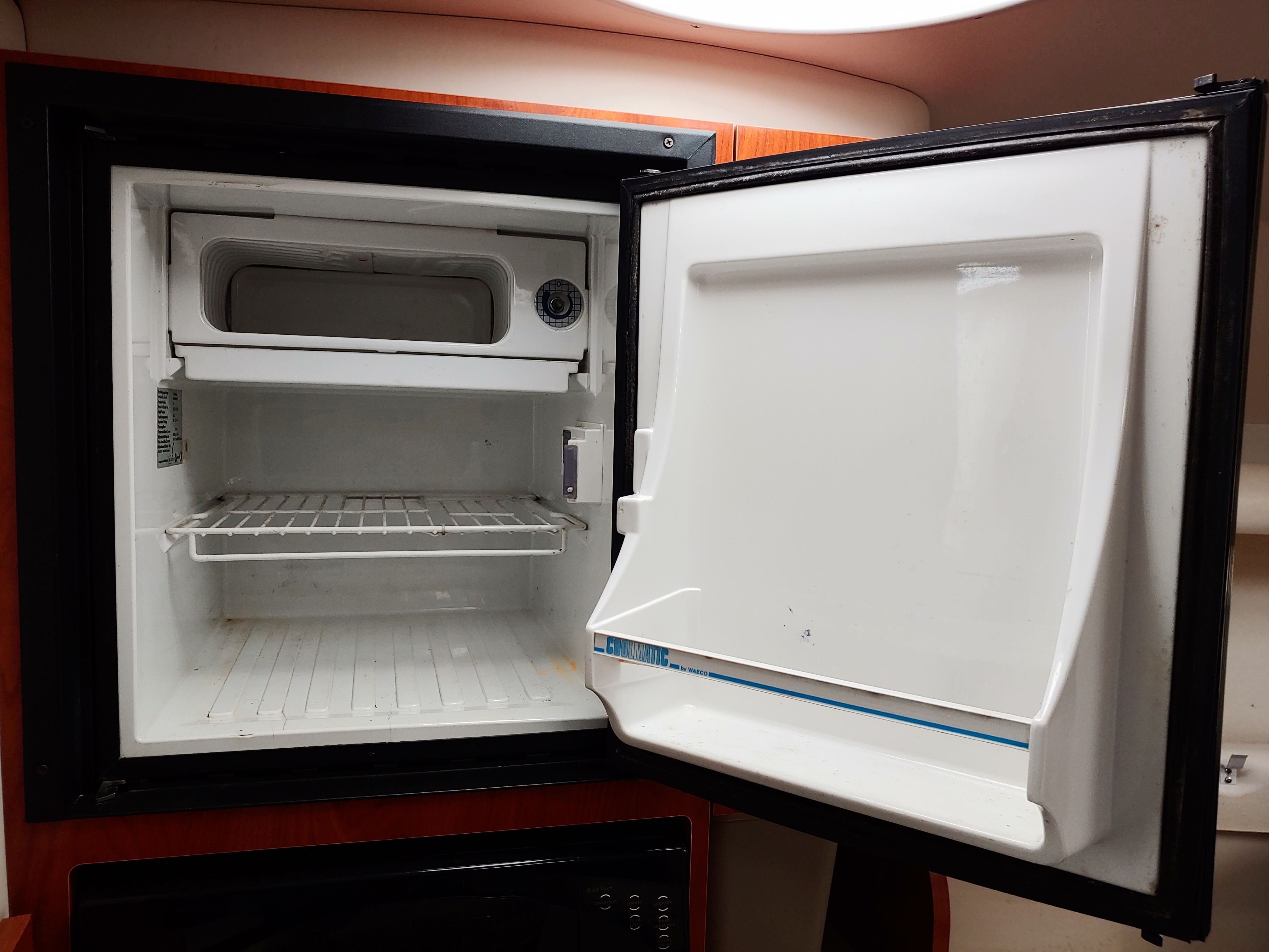 An open refrigerator with an empty shelf and a small freezer compartment.