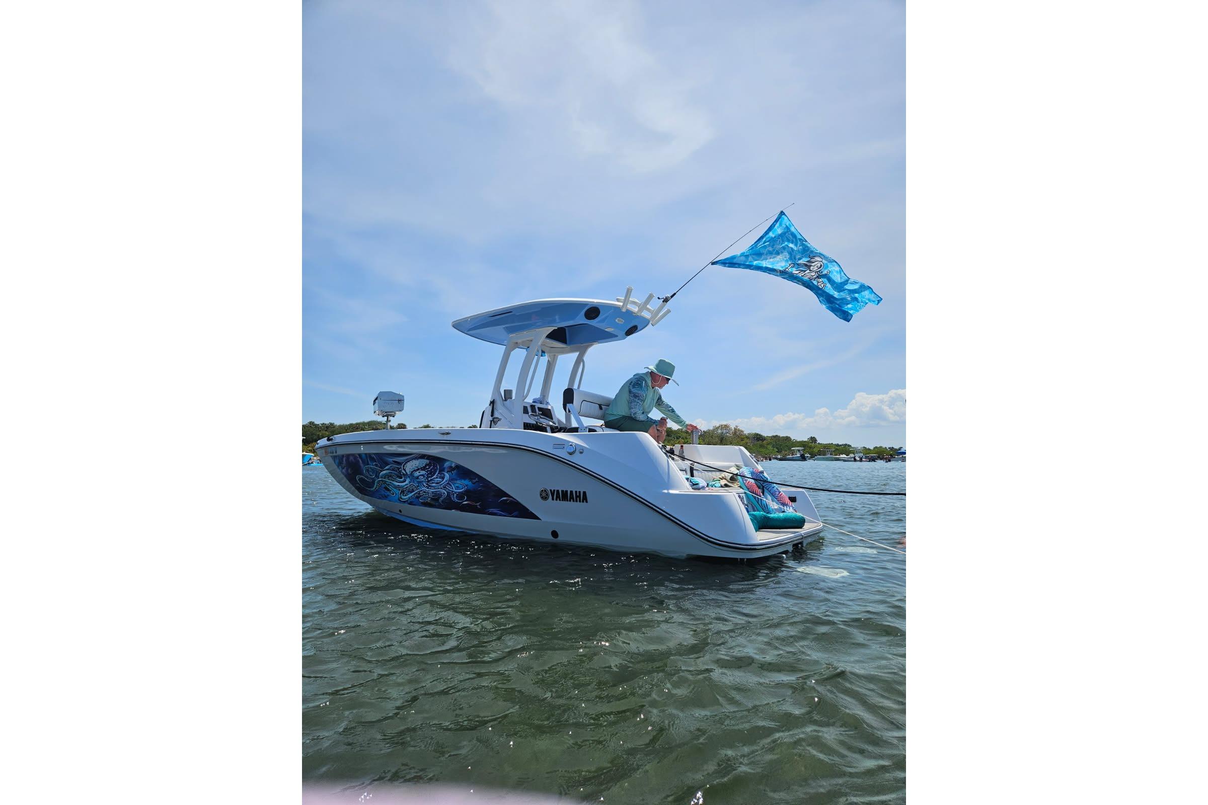 2024 Yamaha Boats 222 FSH Sport E on water, featuring vibrant graphics and a blue flag.
