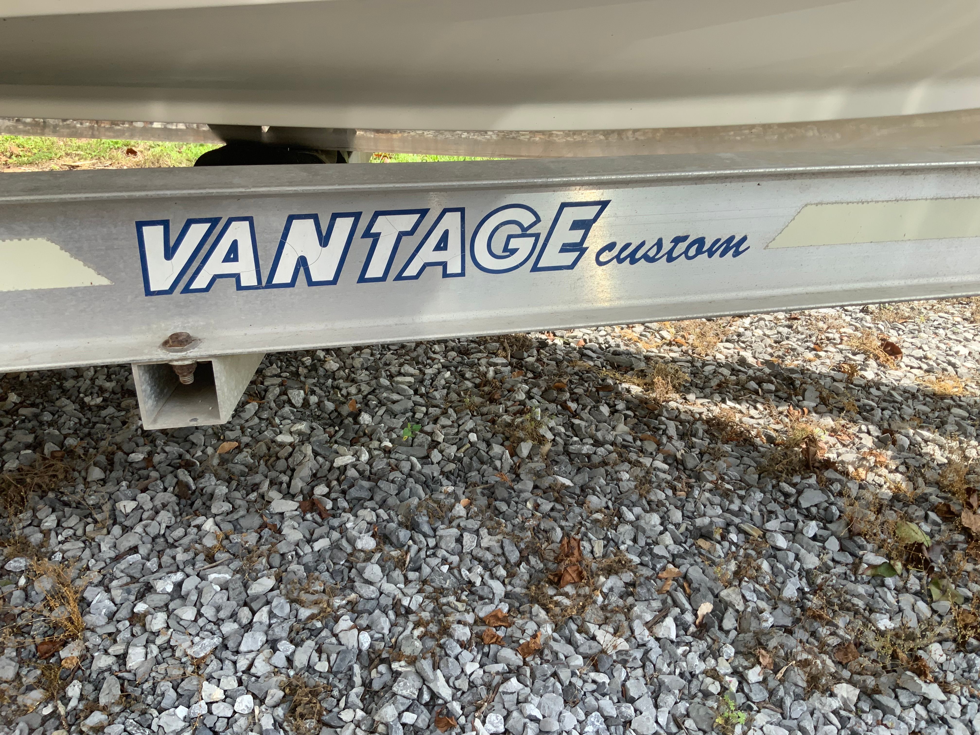 Close-up of a boat trailer with "Vantage Custom" written on it, on a gravel surface.