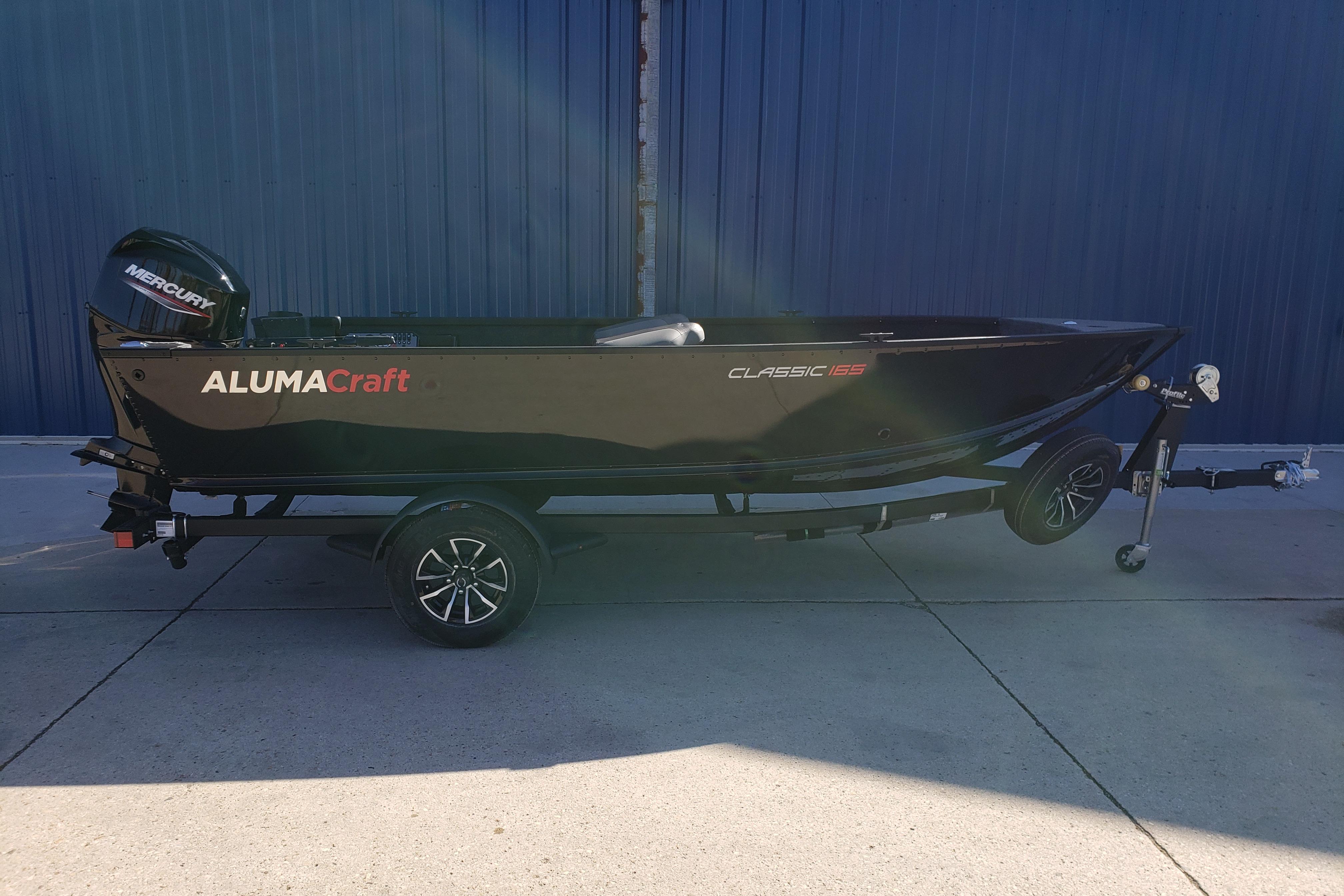 2026 Alumacraft Classic 165 Tiller boat on trailer, side view, outdoors.