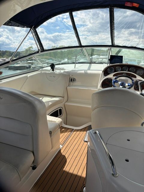 The image shows the cockpit of a 2005 Sea Ray Sundancer 280 with white seats and wood flooring.