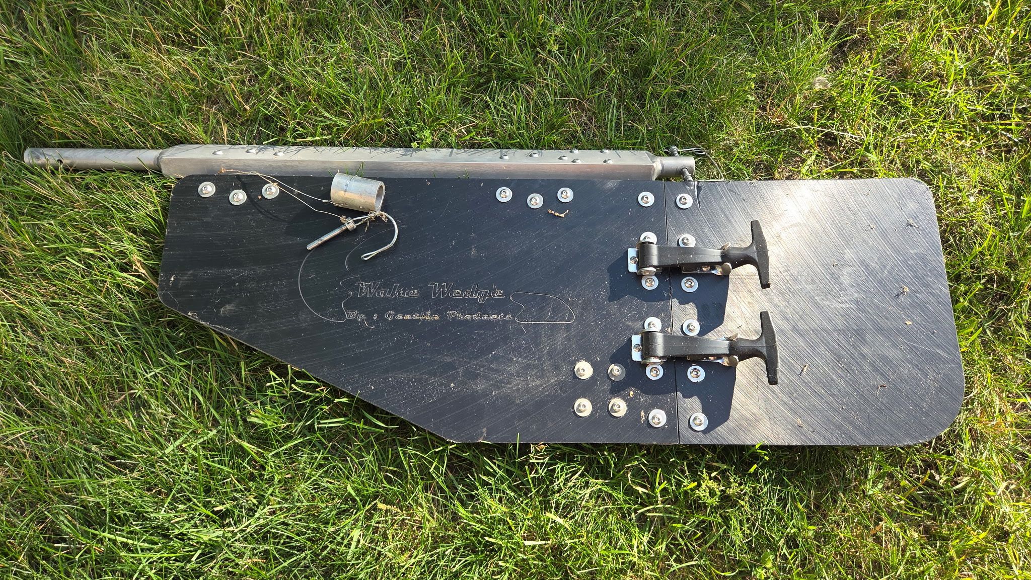 A black boat part with metal fittings lies on grass.