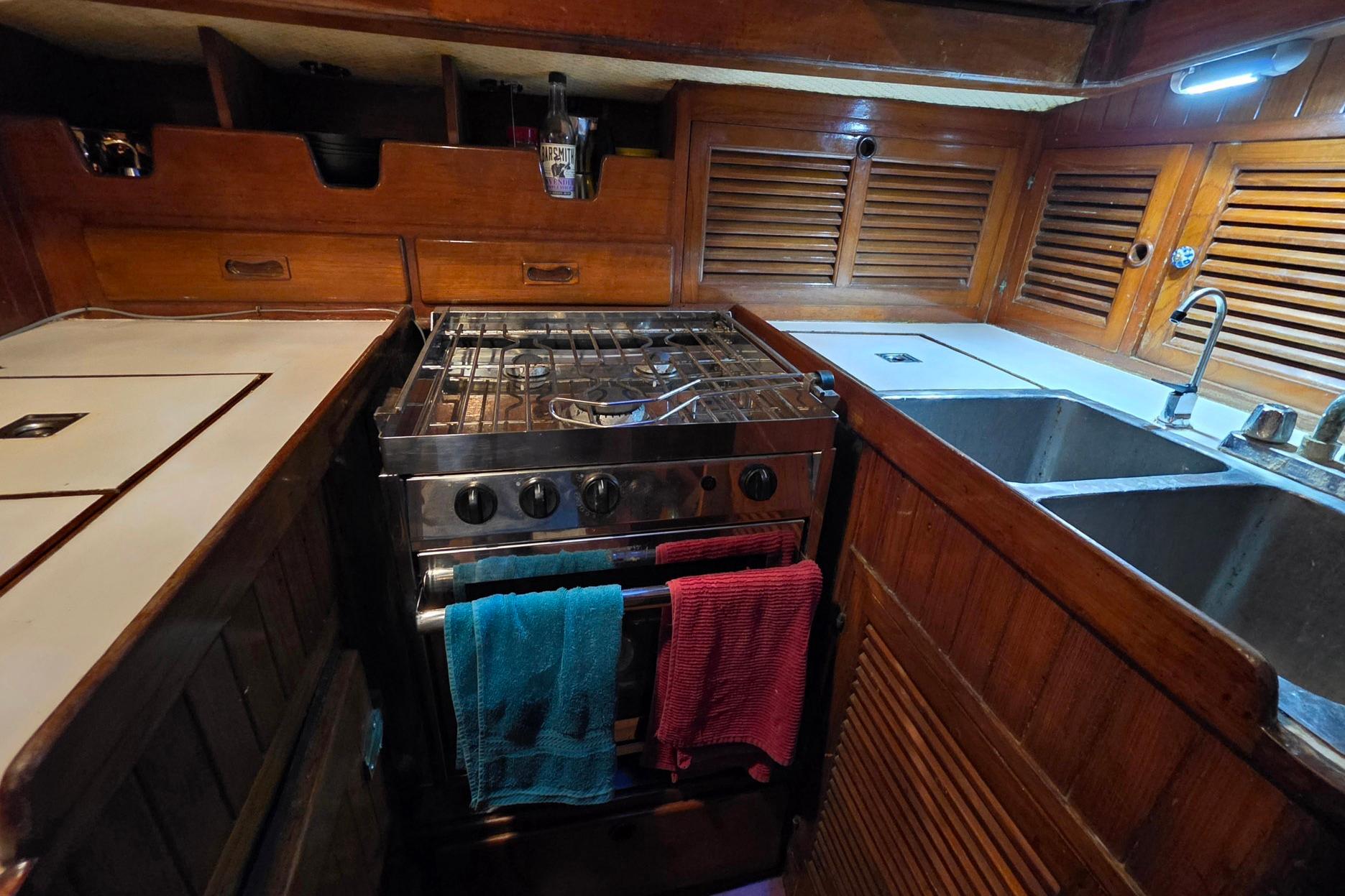 Galley kitchen in 1982 Tayana 37 sailboat with stove, sink, and wooden cabinetry.