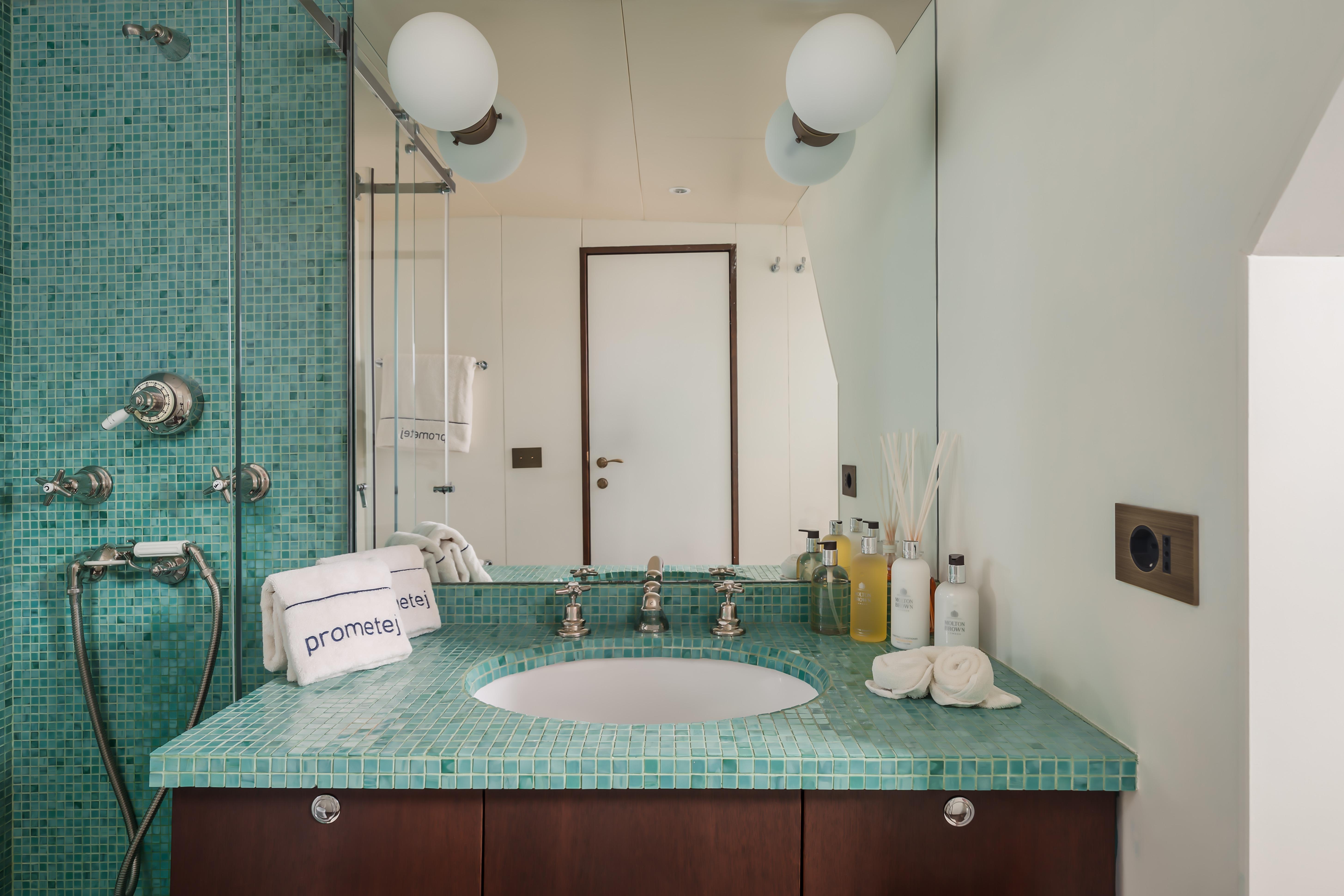 Luxurious bathroom with green mosaic tiles, modern fixtures, and elegant toiletries on a converted 1956 tugboat.