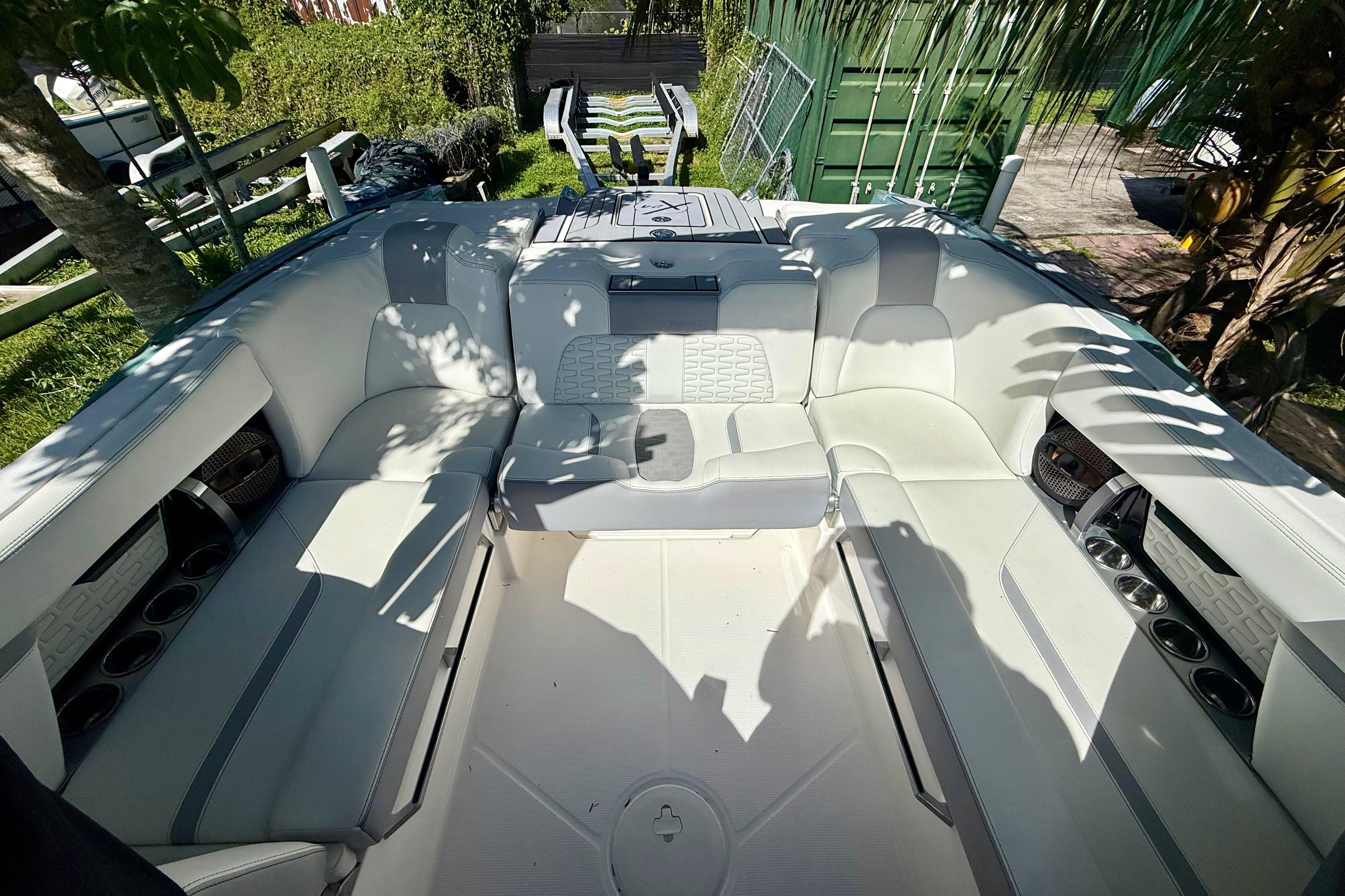 2023 MasterCraft X24 boat interior with white seating and cup holders, surrounded by greenery.