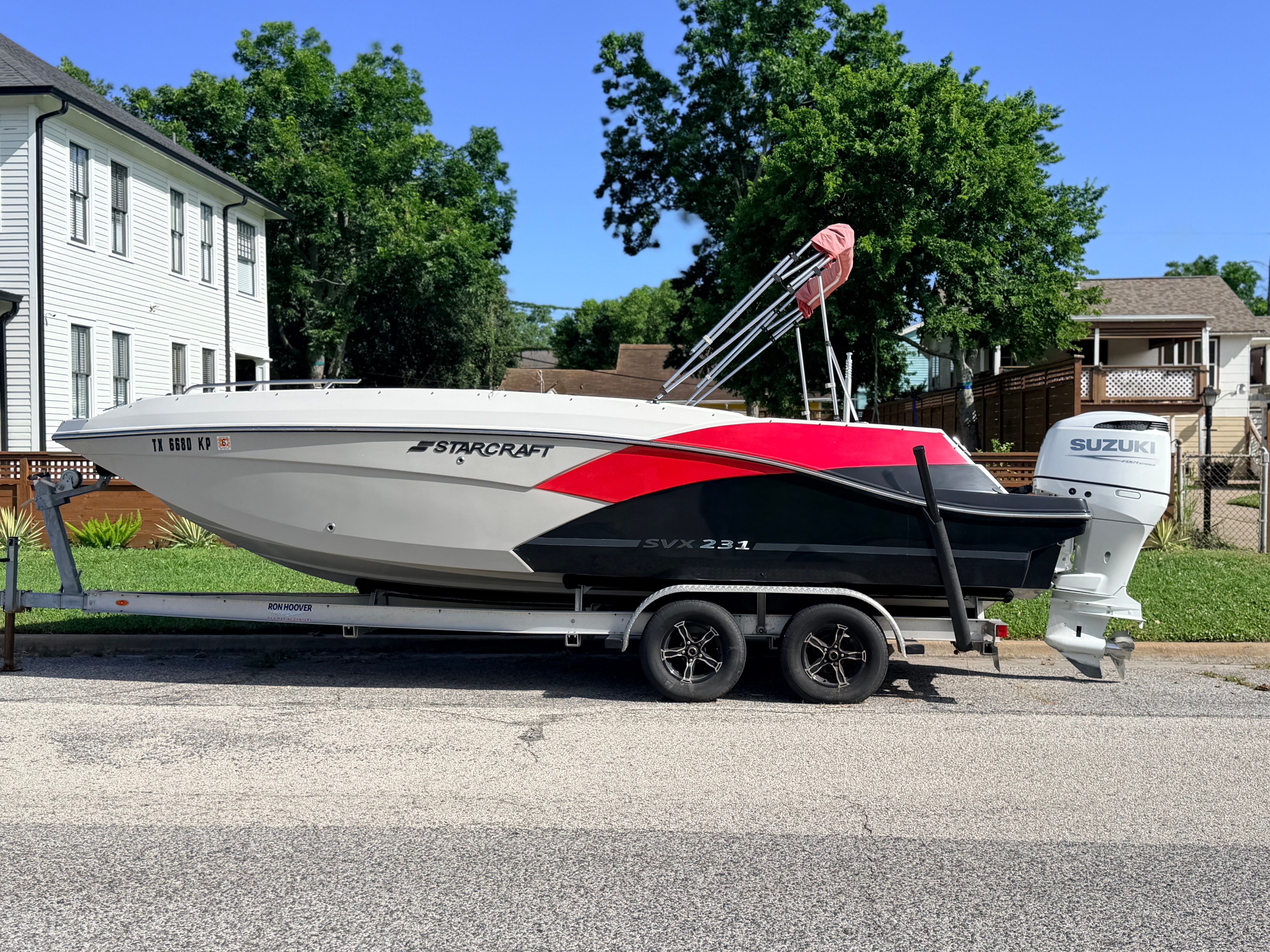 A Starcraft SVX 231 boat on a trailer, parked on a street in front of houses.